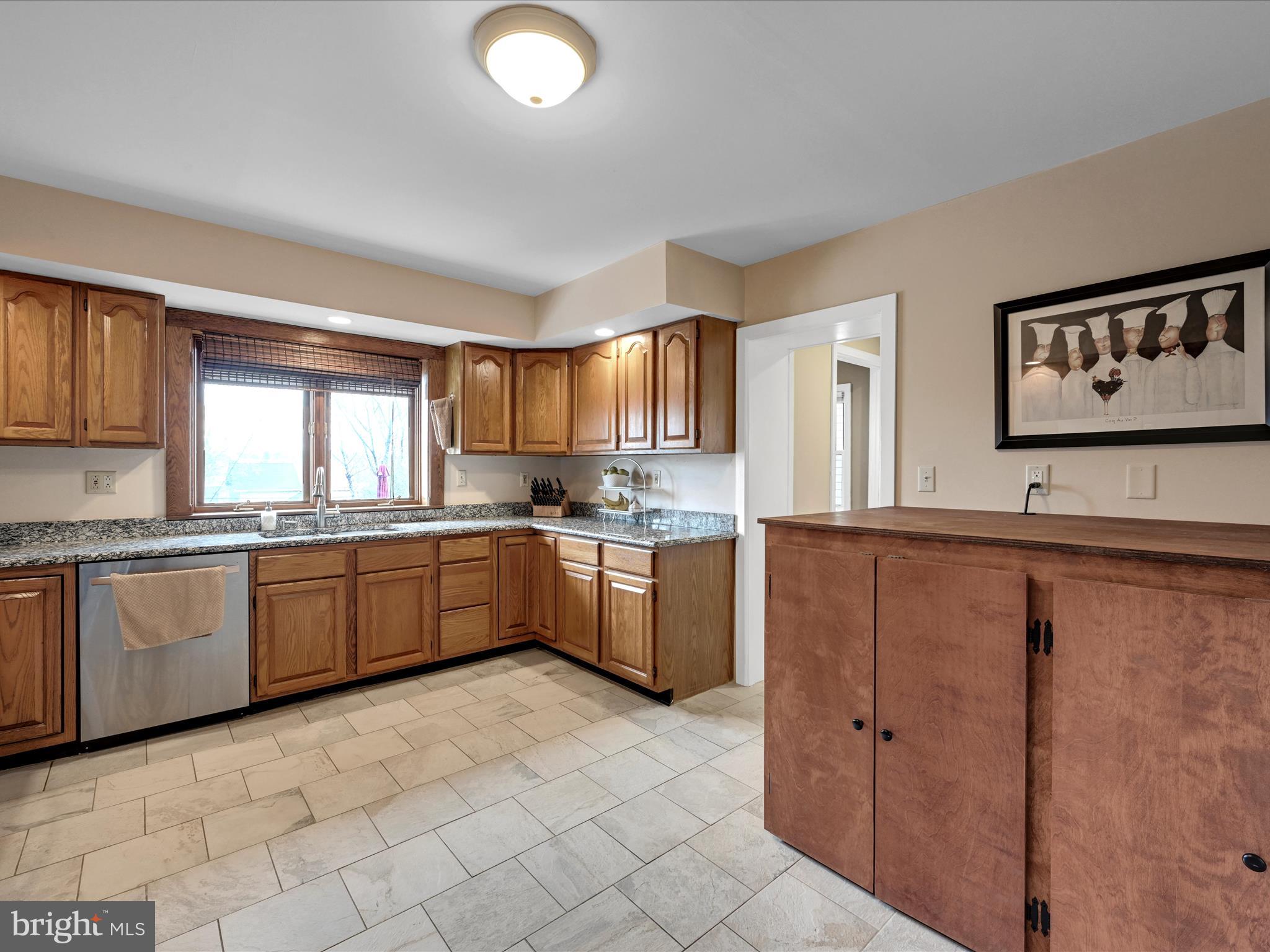 Kitchen with wooden cabinets, granite counters, a window over the sink, and a tiled floor.
