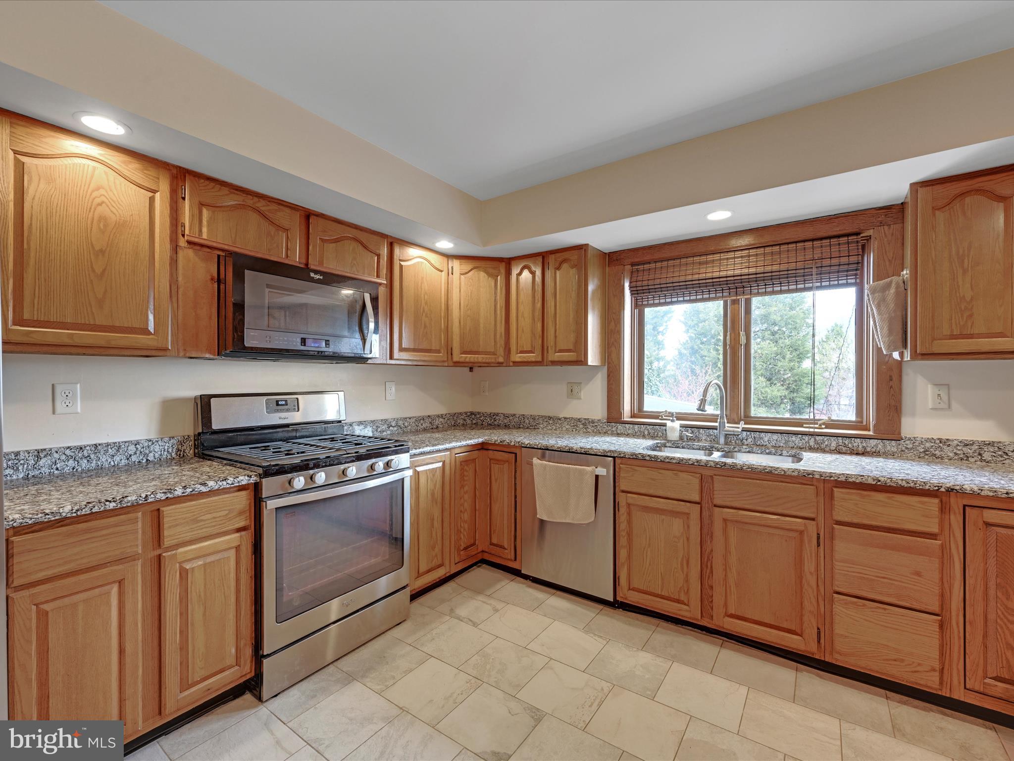 Kitchen with honey-toned wood cabinets, granite counters, stainless steel appliances, and a window over the sink.