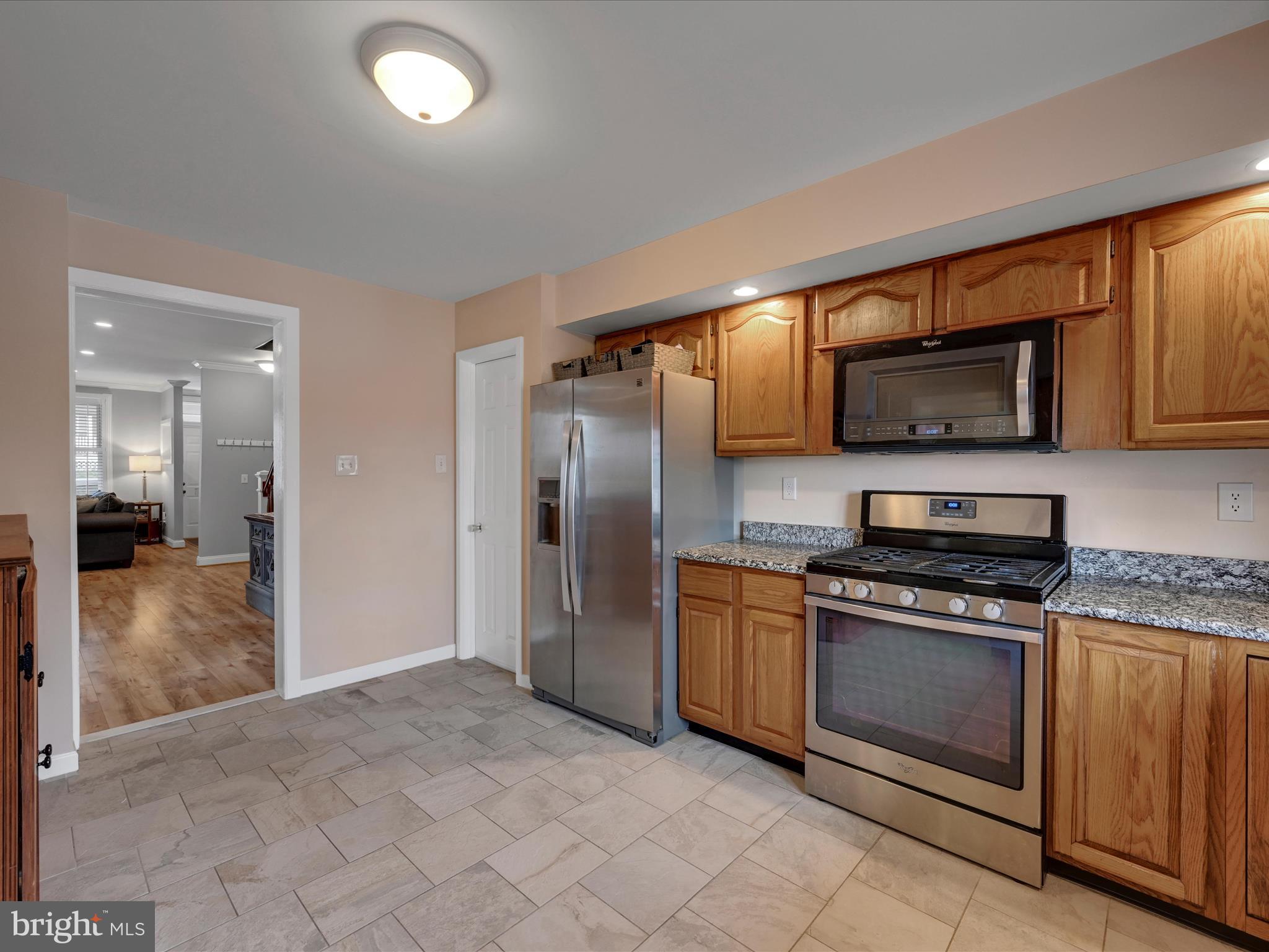 Kitchen with oak cabinets, granite counters, stainless steel appliances, and gray tile flooring.