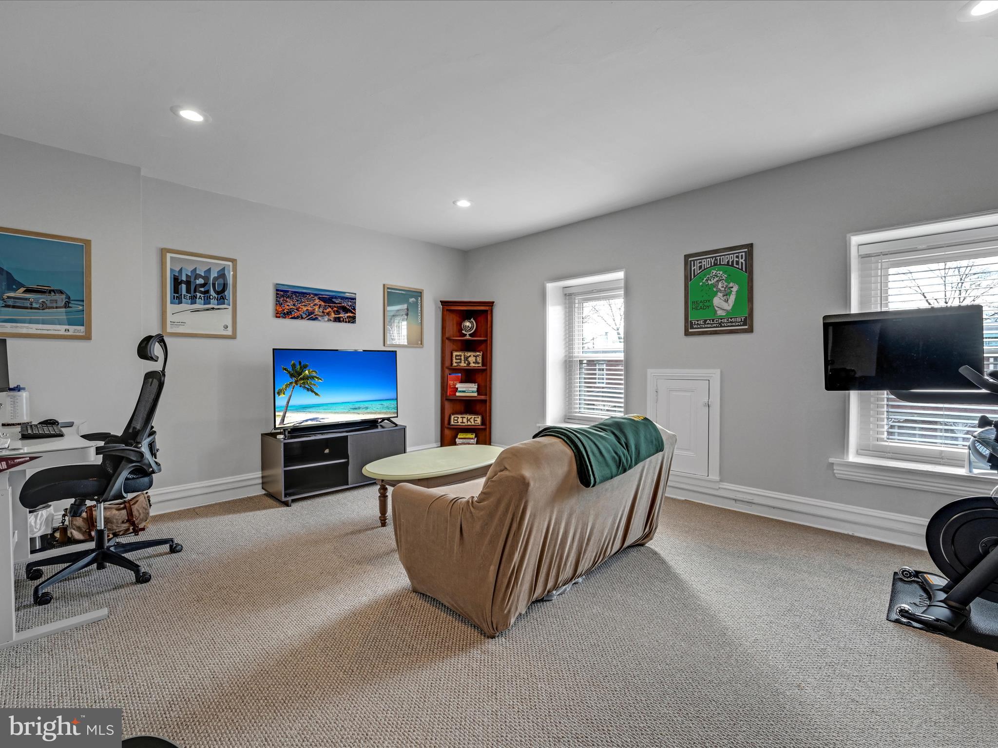 Home office and lounge with a sofa, desk, television, and exercise equipment.