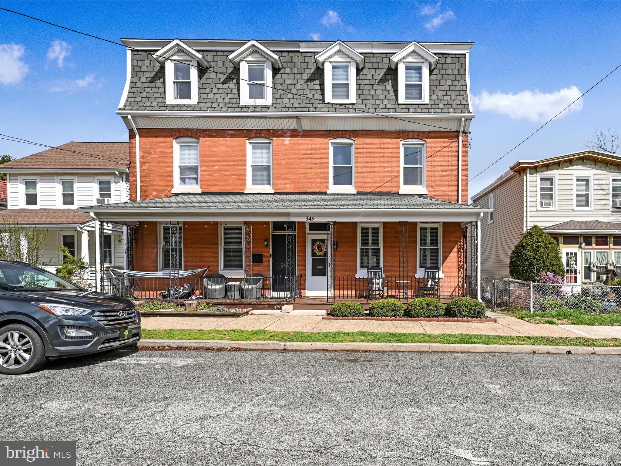 Red brick three-story house with a mansard roof, four dormers, and a furnished covered porch.