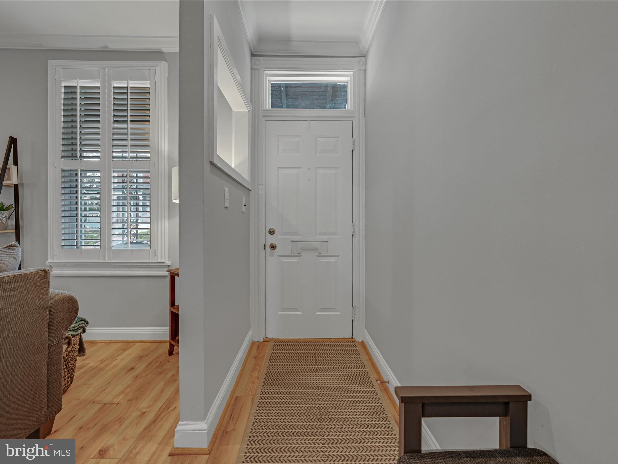 Entryway with a white paneled front door, transom window, patterned runner, and shuttered window.