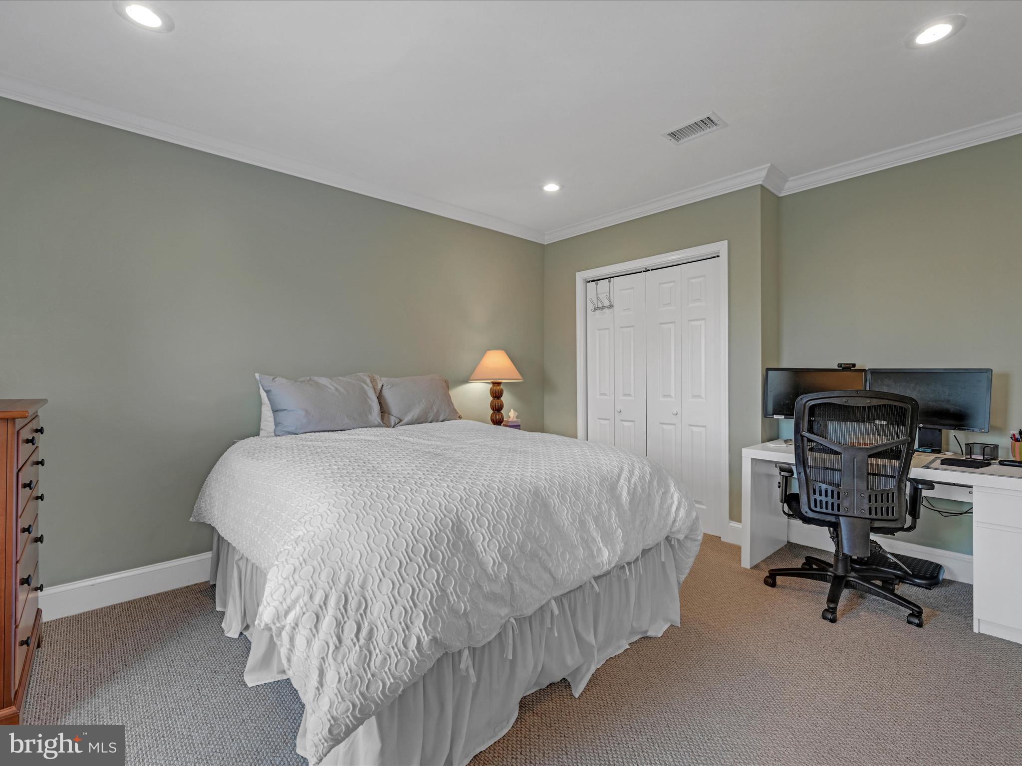 Bedroom with a white quilted bed and a desk with dual monitors.