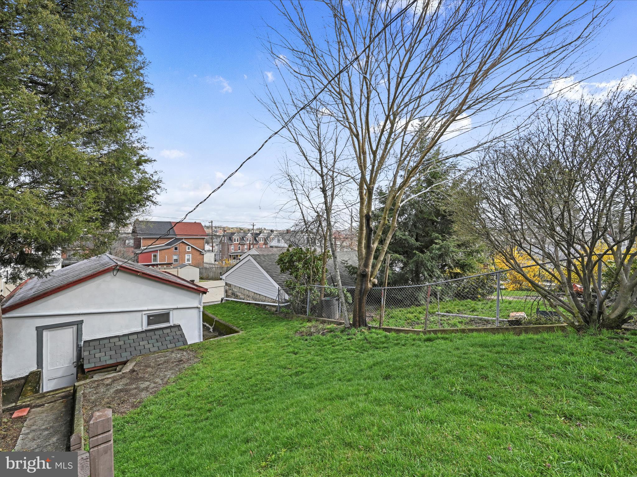 Sloping grassy backyard with a chain-link fence, mature trees, and neighborhood rooftops beyond.