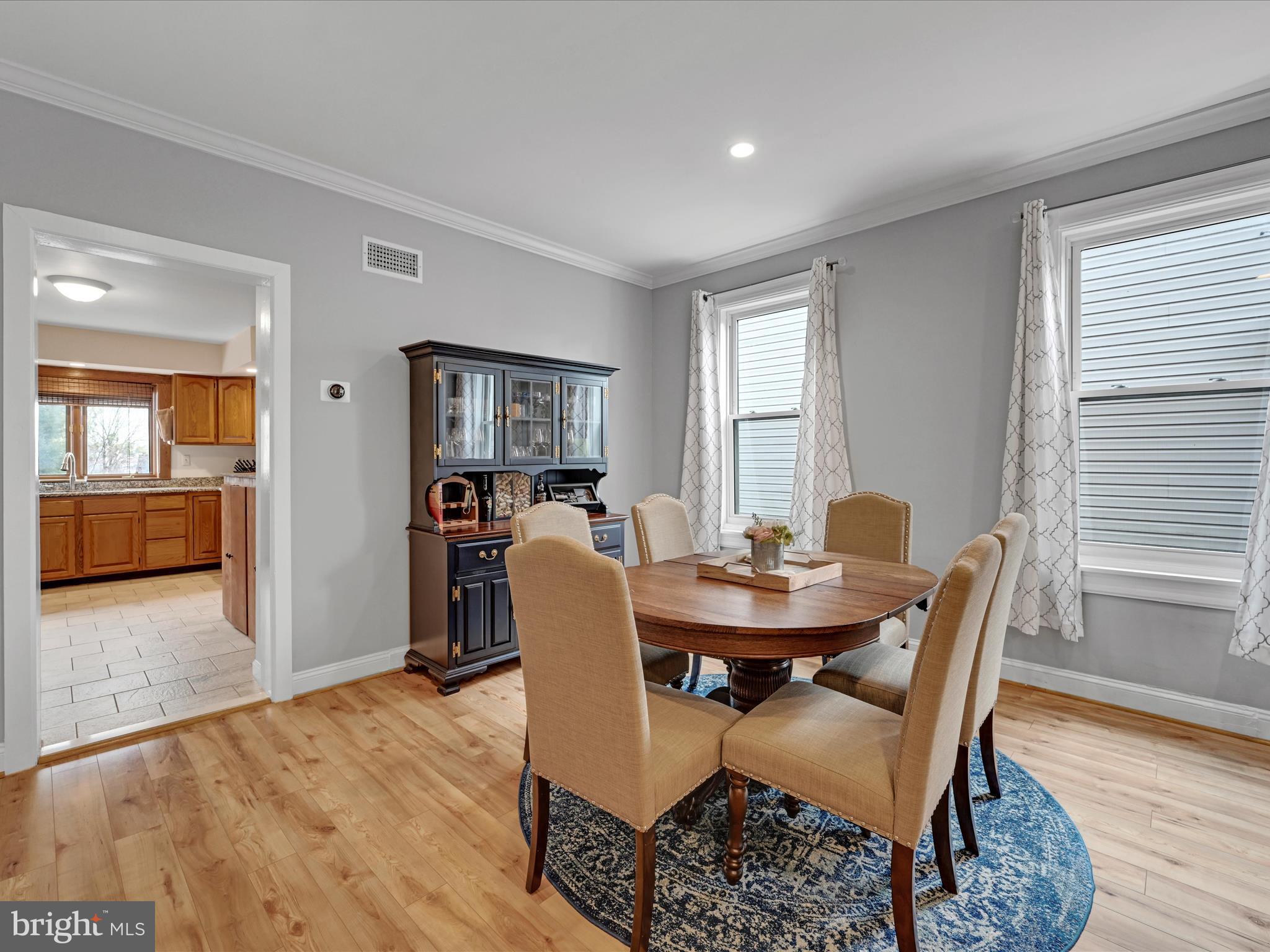 Dining room with a round wood table, beige chairs, and a dark china cabinet beside the kitchen.