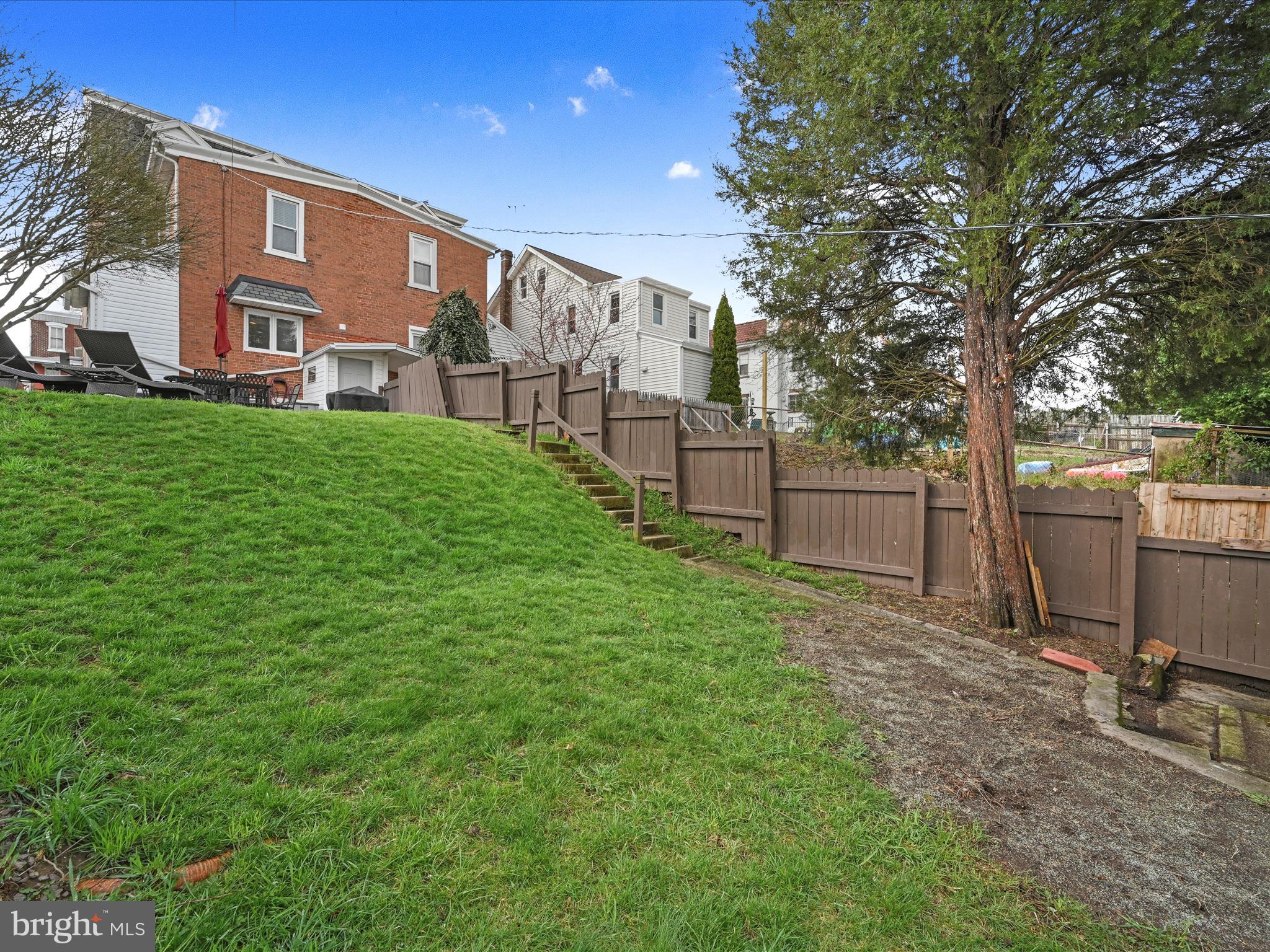 Rear of a red brick house above a sloping lawn, with fenced steps and a large tree.