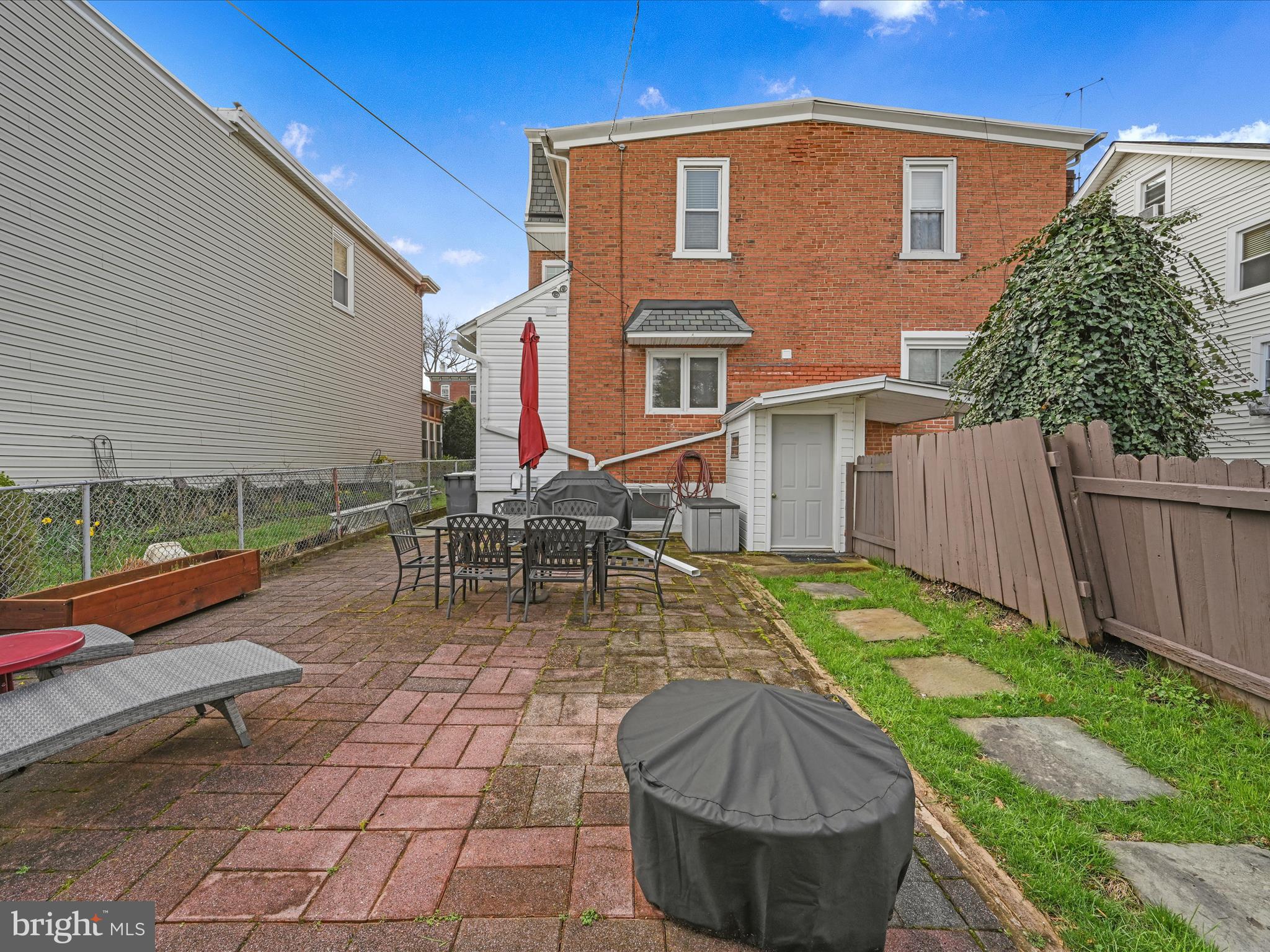 Brick home’s backyard patio with outdoor dining furniture and a small fenced lawn.