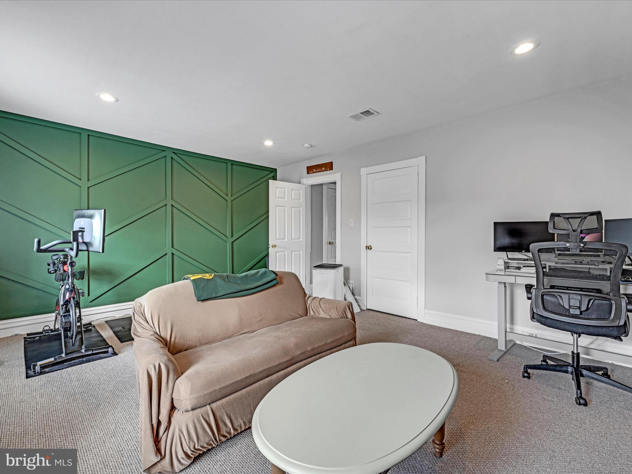 Flex room with a green geometric accent wall, sofa, exercise bike, and desk.