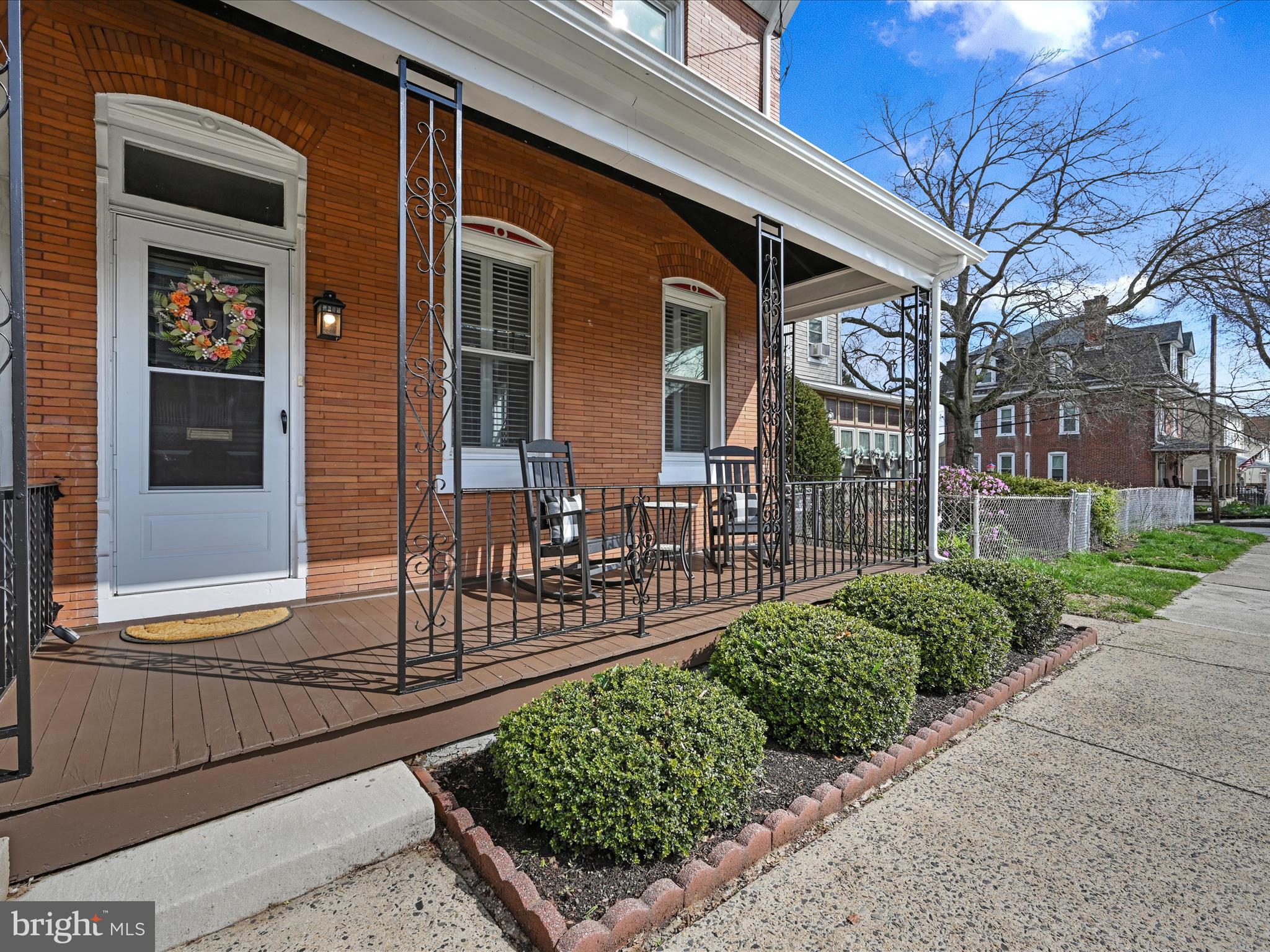 Red-brick home with a covered front porch, decorative iron railings, and neatly trimmed shrubs.