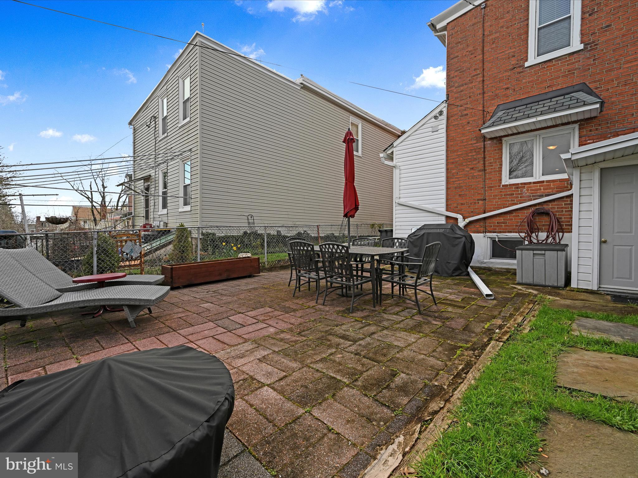 Paved backyard patio with outdoor dining furniture, lounge chairs, and a covered grill.