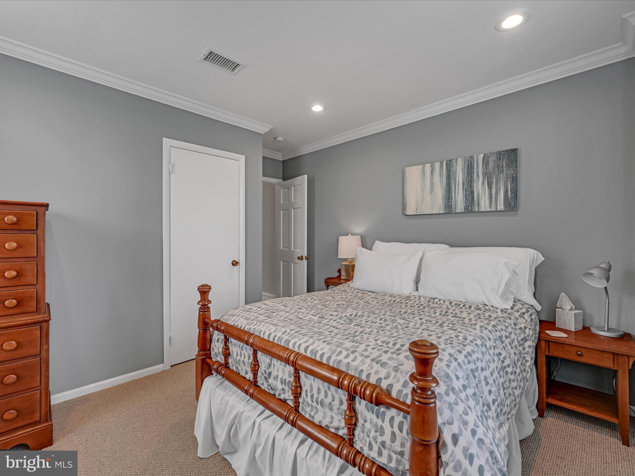 Furnished bedroom with a carved wooden bed, patterned bedding, gray walls, and beige carpet.