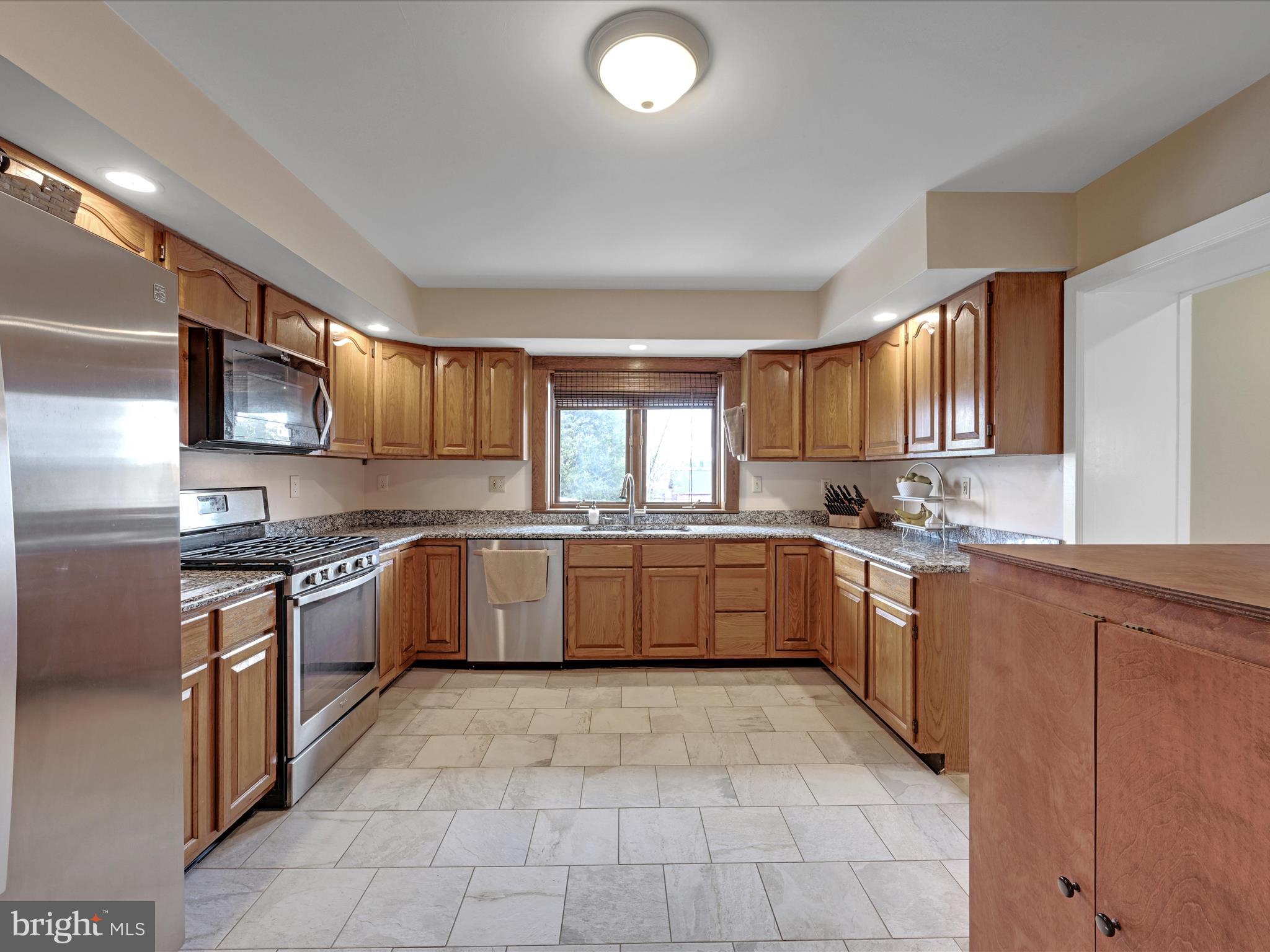 U-shaped kitchen with warm wood cabinets, granite counters, stainless appliances, and a window above the sink.