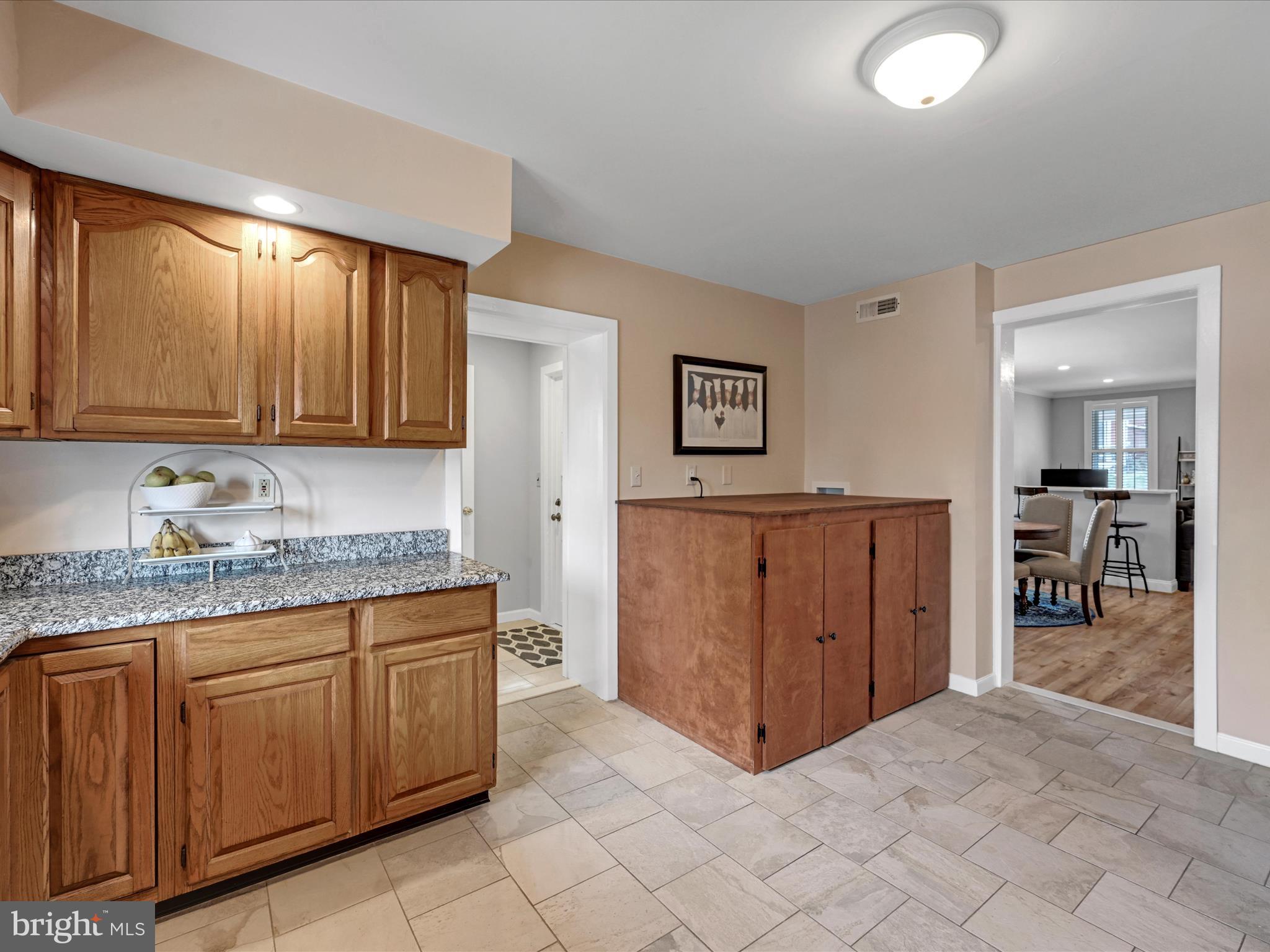 Kitchen with oak cabinetry, granite counters, tiled floor, and a wooden cabinet beside an adjoining room.