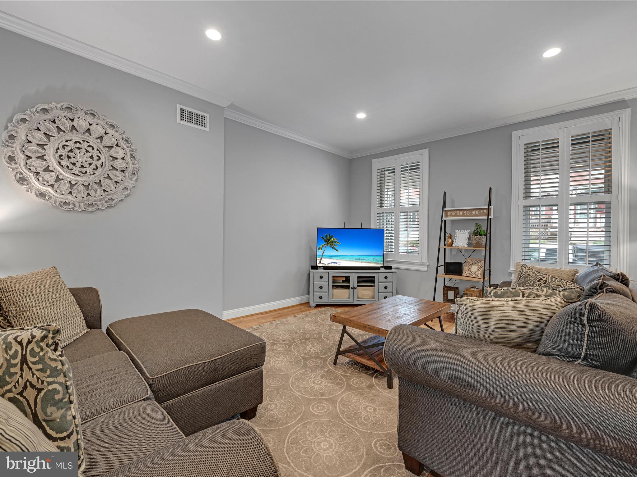 Living room with gray sofas, a wooden coffee table, patterned rug, and shuttered windows.