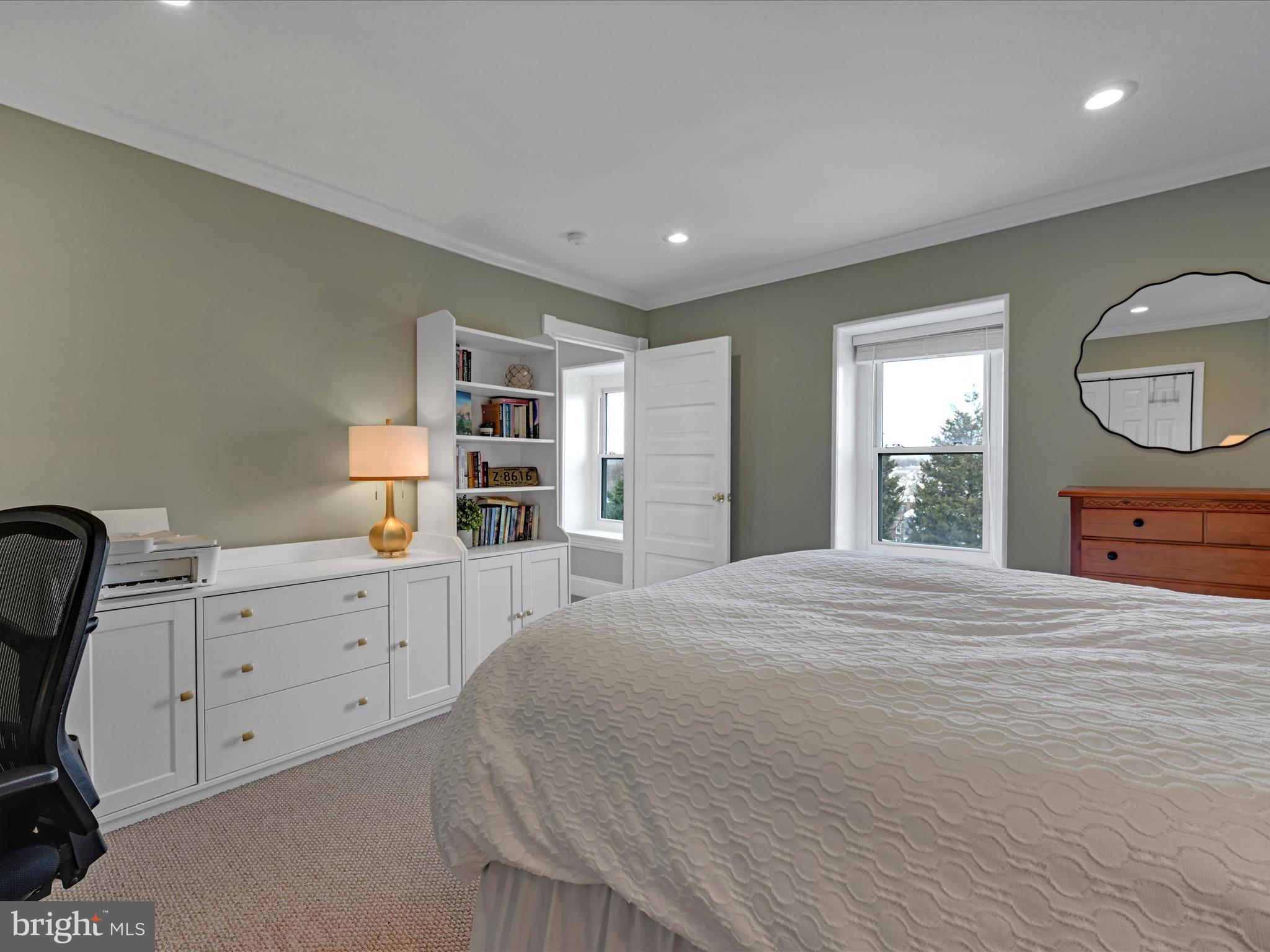 Furnished bedroom with white built-in bookshelves, a large bed, and two windows.