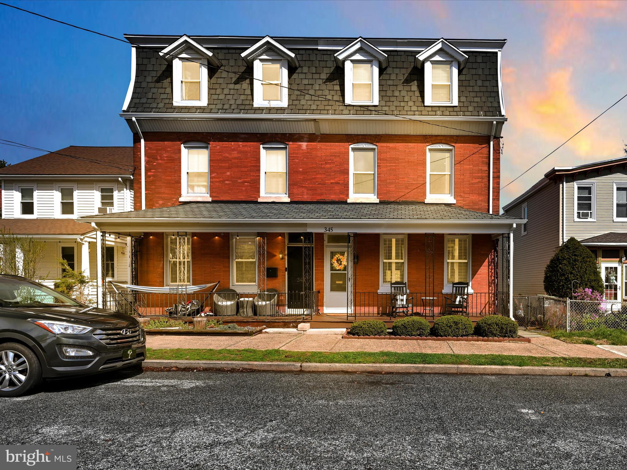 Red-brick house with a covered porch, four roof dormers, and 345 above the entrance.