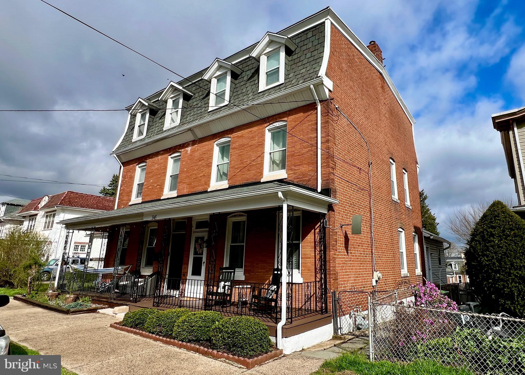 Red-brick home with a steep gray mansard roof, white-trimmed dormers, and a covered porch.