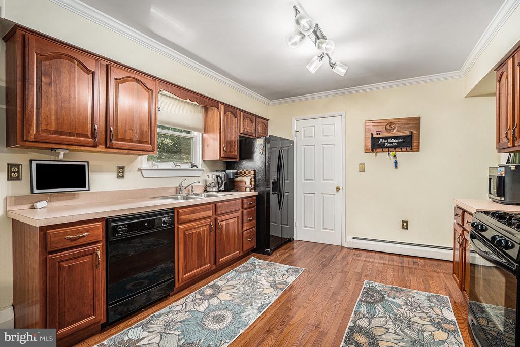 Kitchen with reddish-brown wood cabinets, black appliances, and two floral floor runners.