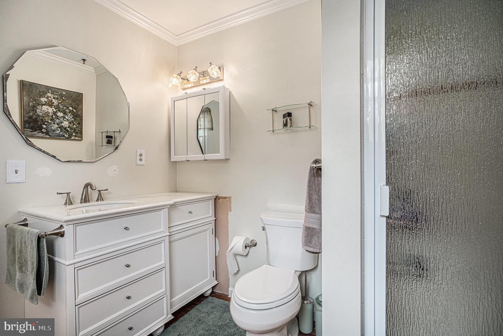 Bathroom with a white paneled vanity, large faceted mirror, toilet, and textured-glass shower enclosure.