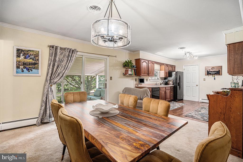 Dining room with a large wood table and chandelier beside an open kitchen and sliding glass doors.
