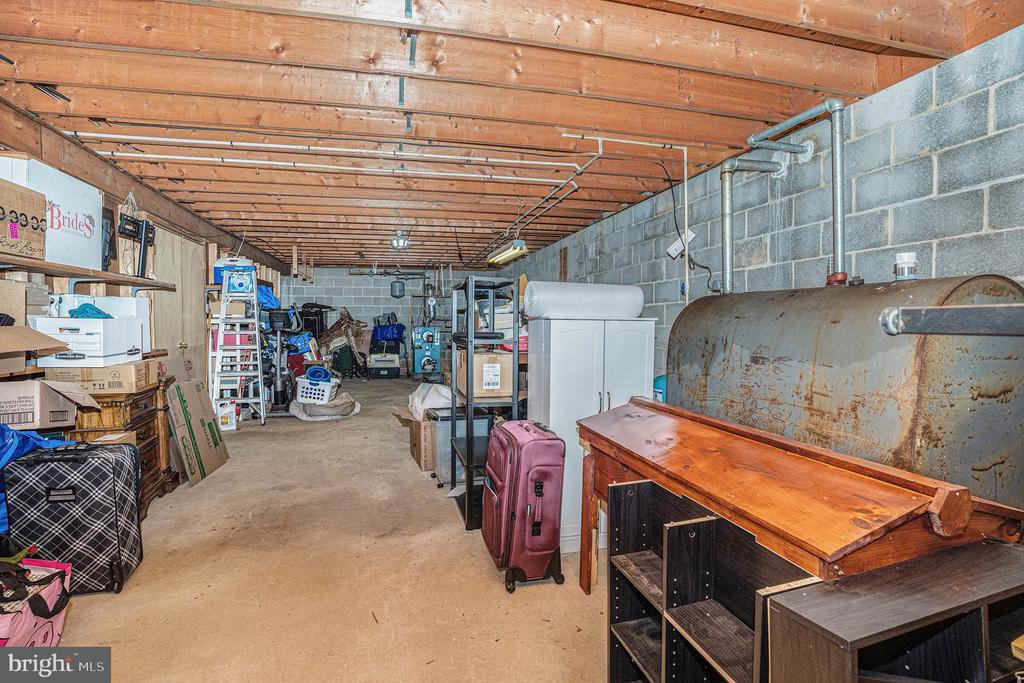 Unfinished basement storage area with exposed ceiling joists, block walls, and a large cylindrical tank.