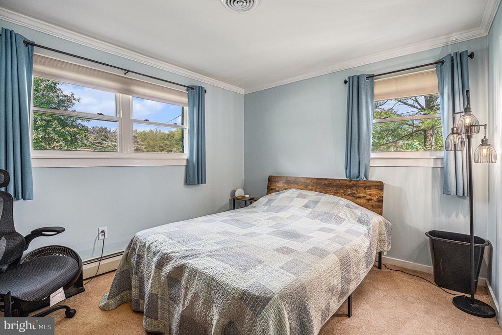 Bedroom with a patchwork-quilt bed, pale blue walls, and two windows with blue curtains.