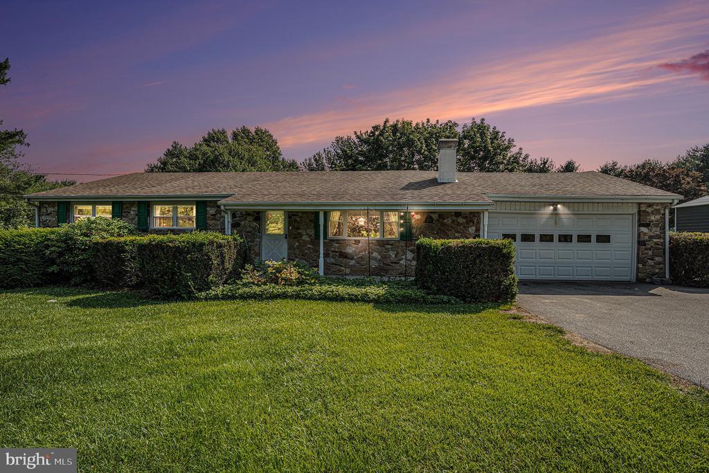 Single-story stone-front home with green shutters and an attached garage at sunset.