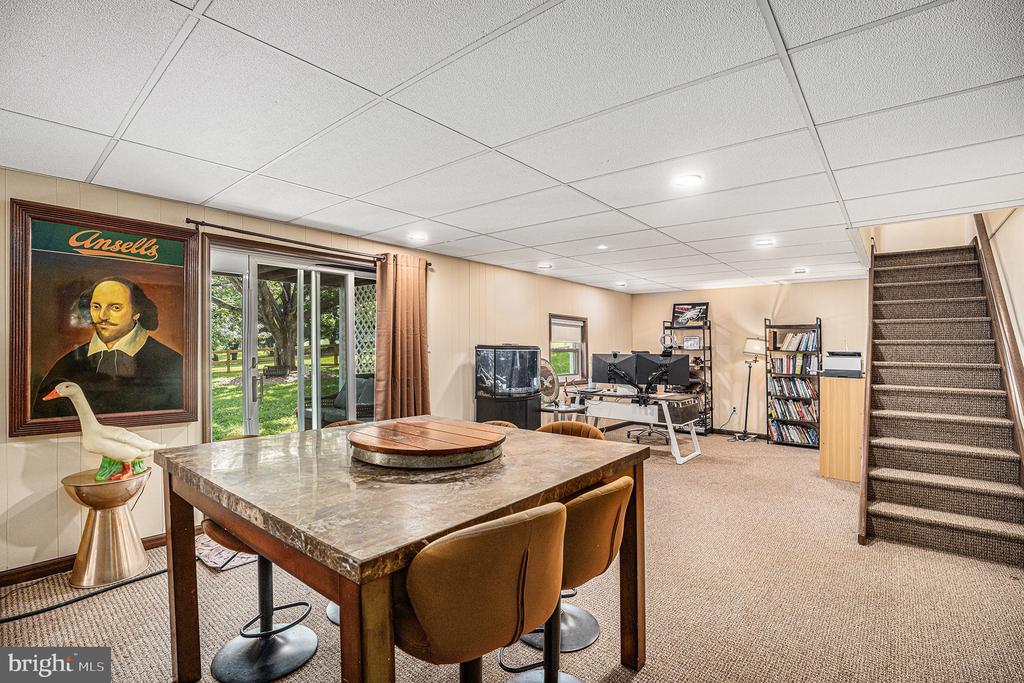 Furnished lower-level room with a stone-topped table, computer workspace, carpeted stairs, and sliding glass doors.