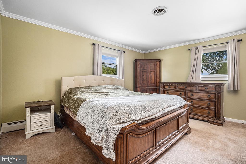 Bedroom with a large wooden bed and matching dresser beneath curtained windows.