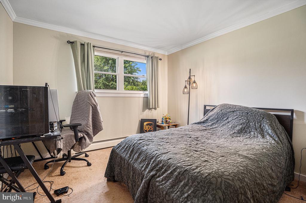 Bedroom with a gray quilted bed, computer workstation, and window overlooking trees.