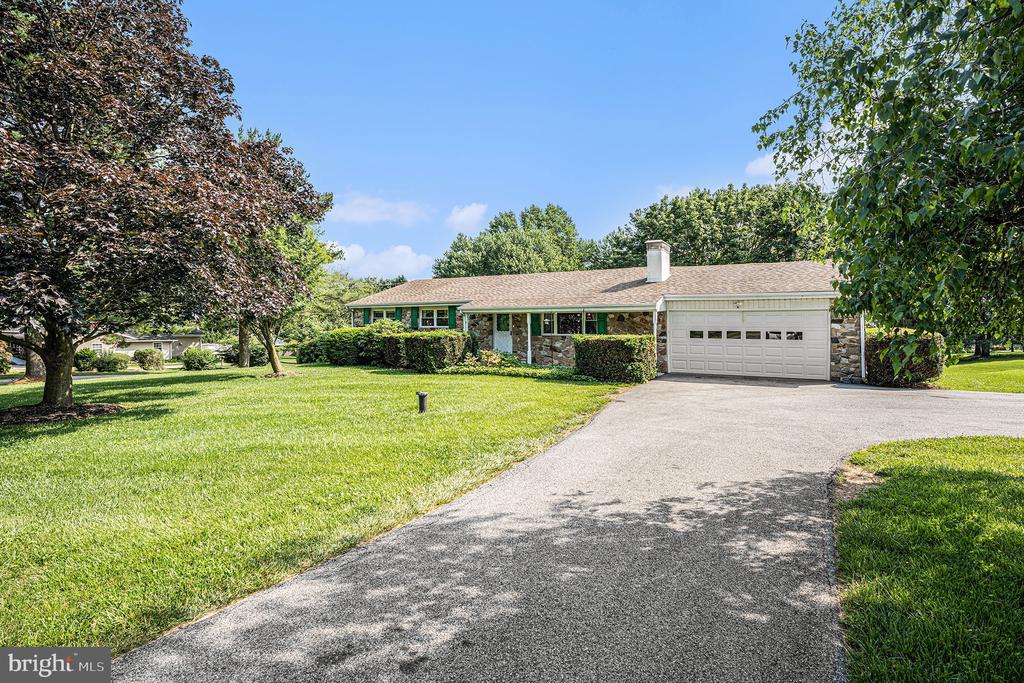 Single-story ranch home with stone accents, attached garage, wide driveway, and mature trees.