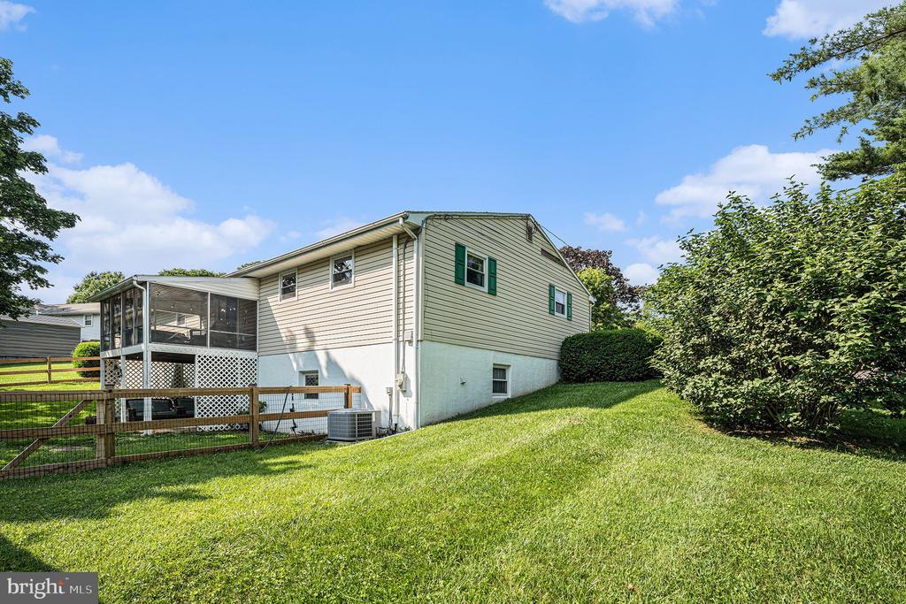 Home exterior with screened porch, green shutters, and a sloping fenced lawn.