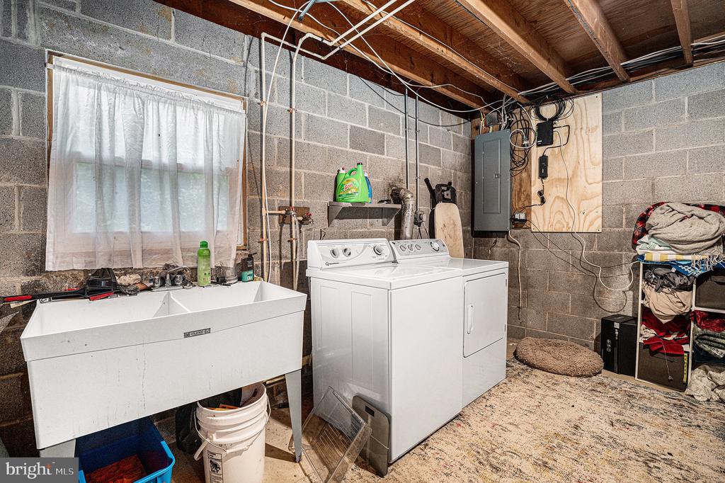 Basement laundry room with a deep utility sink, washer, dryer, and exposed ceiling joists.