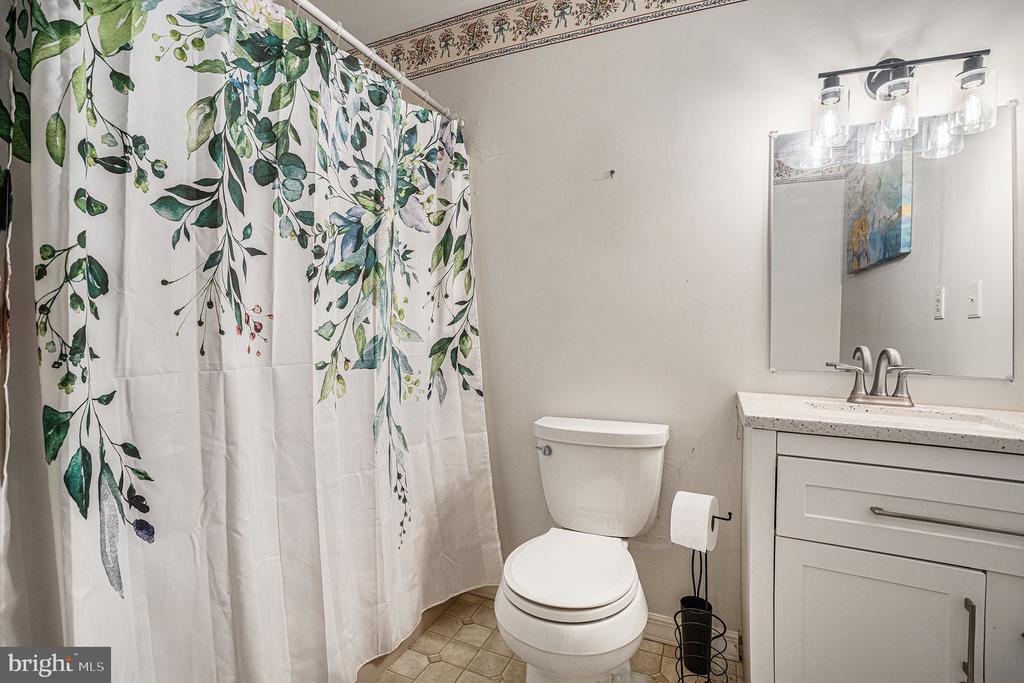Bathroom with a leafy botanical shower curtain beside a toilet and white vanity.