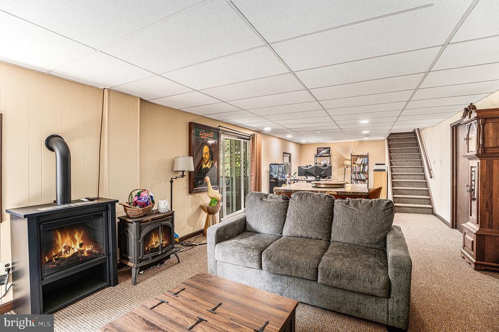 Basement family room with a gray sectional, two wood stoves, and stairs.