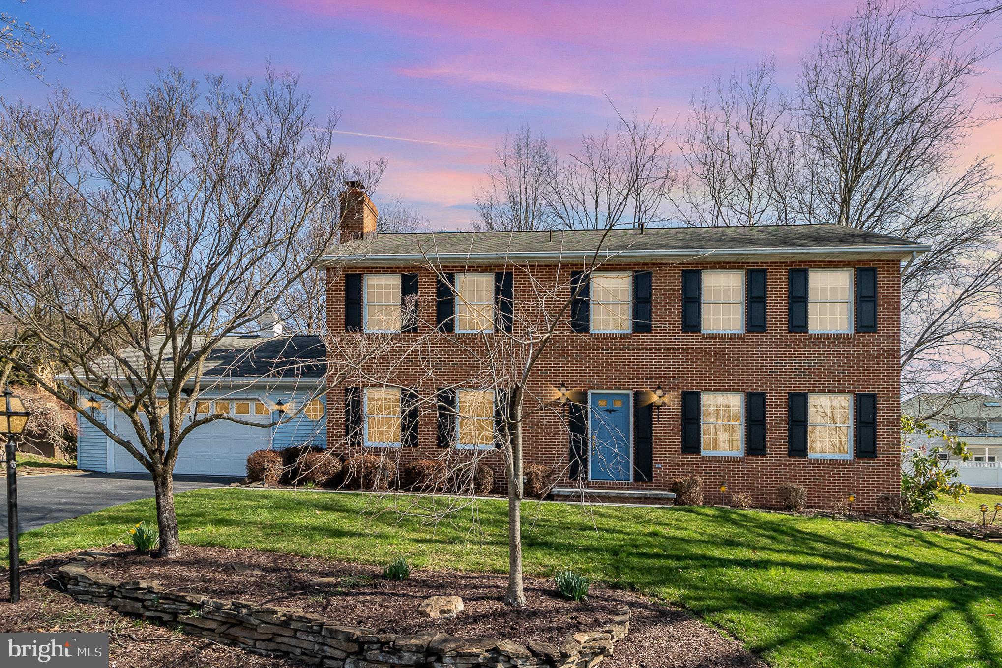 Two-story brick house with a blue front door, black shutters, and attached garage at dusk.