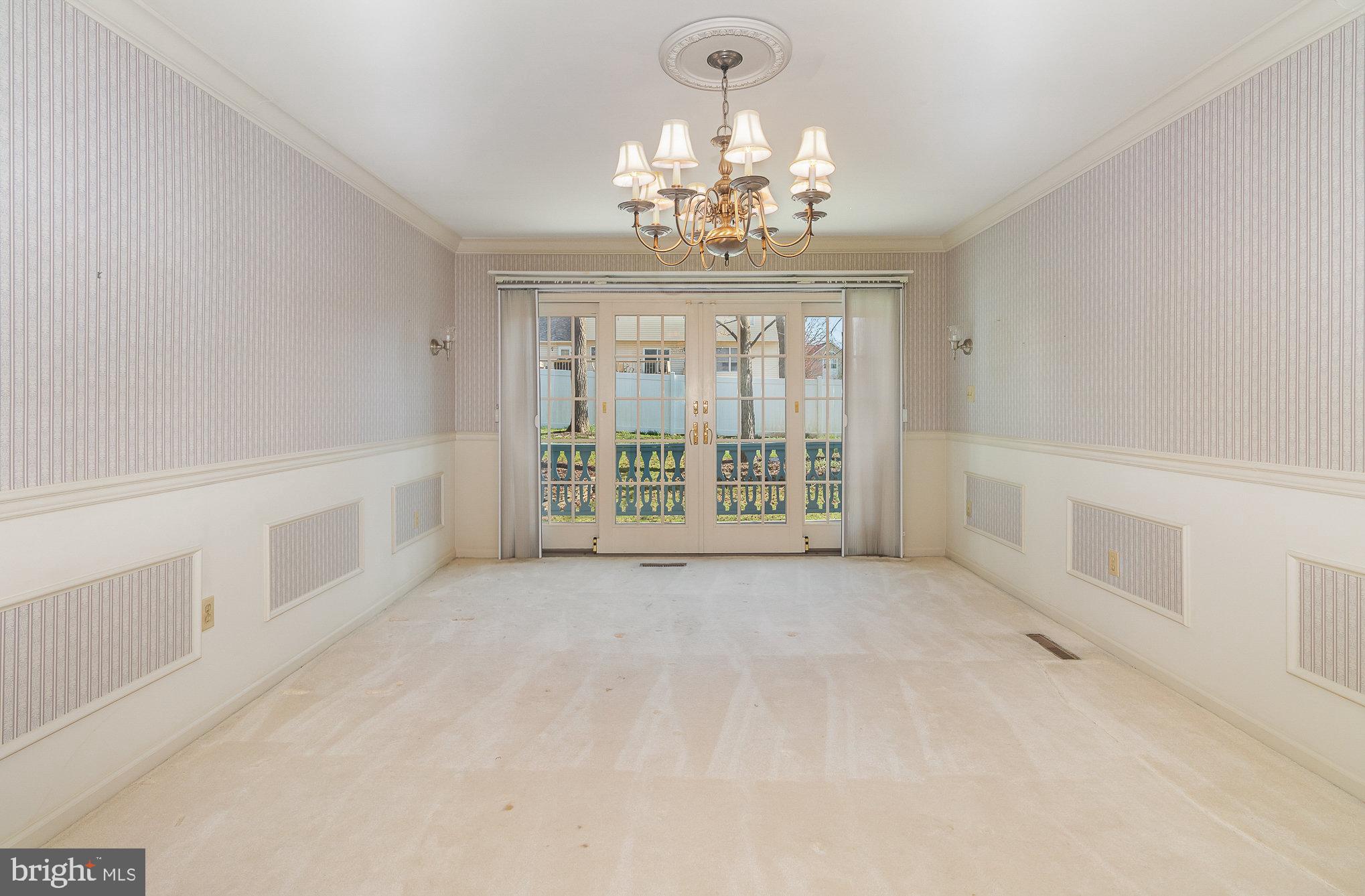 Empty dining room with a brass chandelier and French doors opening to a balcony.