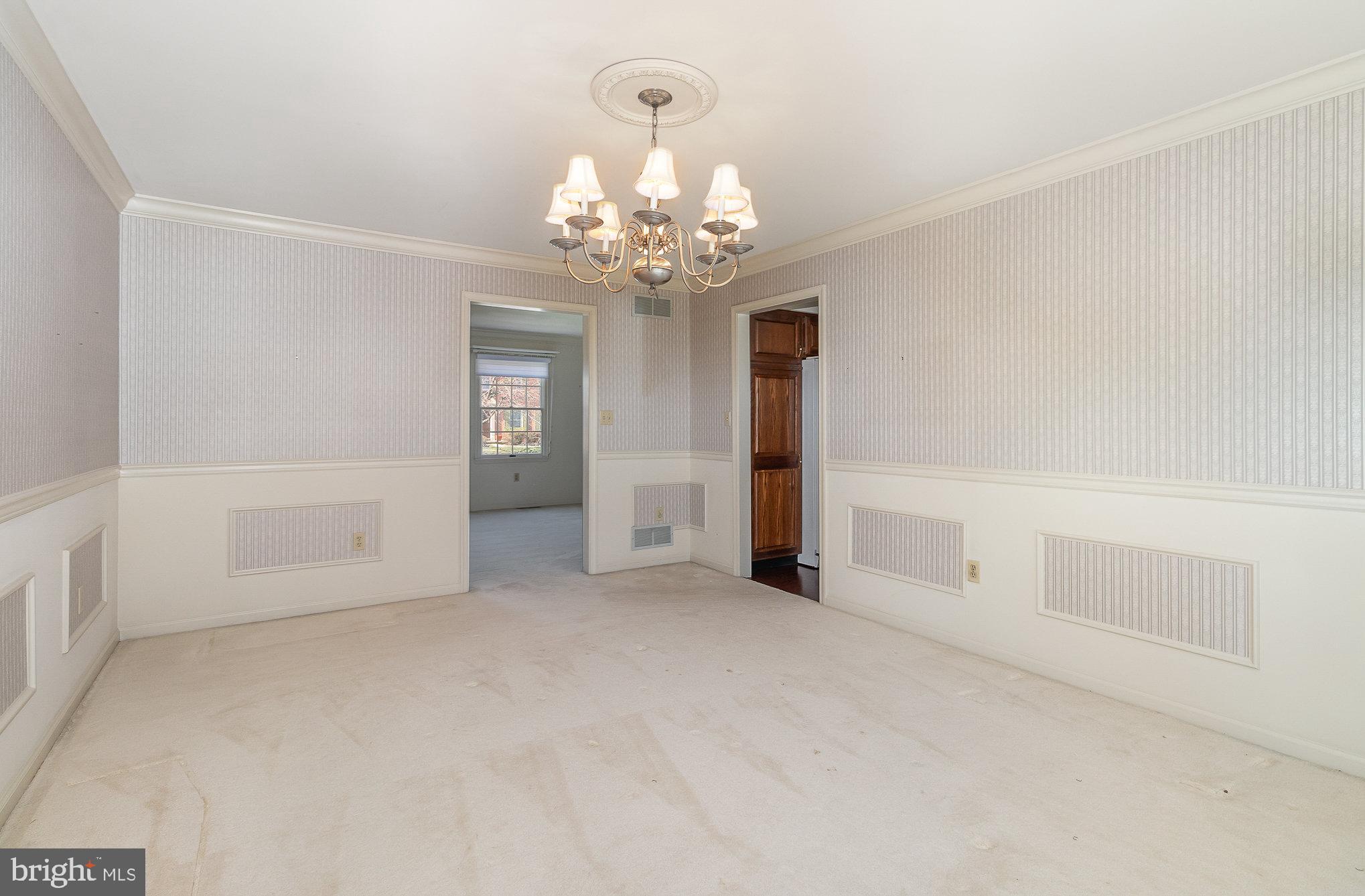 Vacant dining room with striped wallpaper, cream carpet, and a brass chandelier.