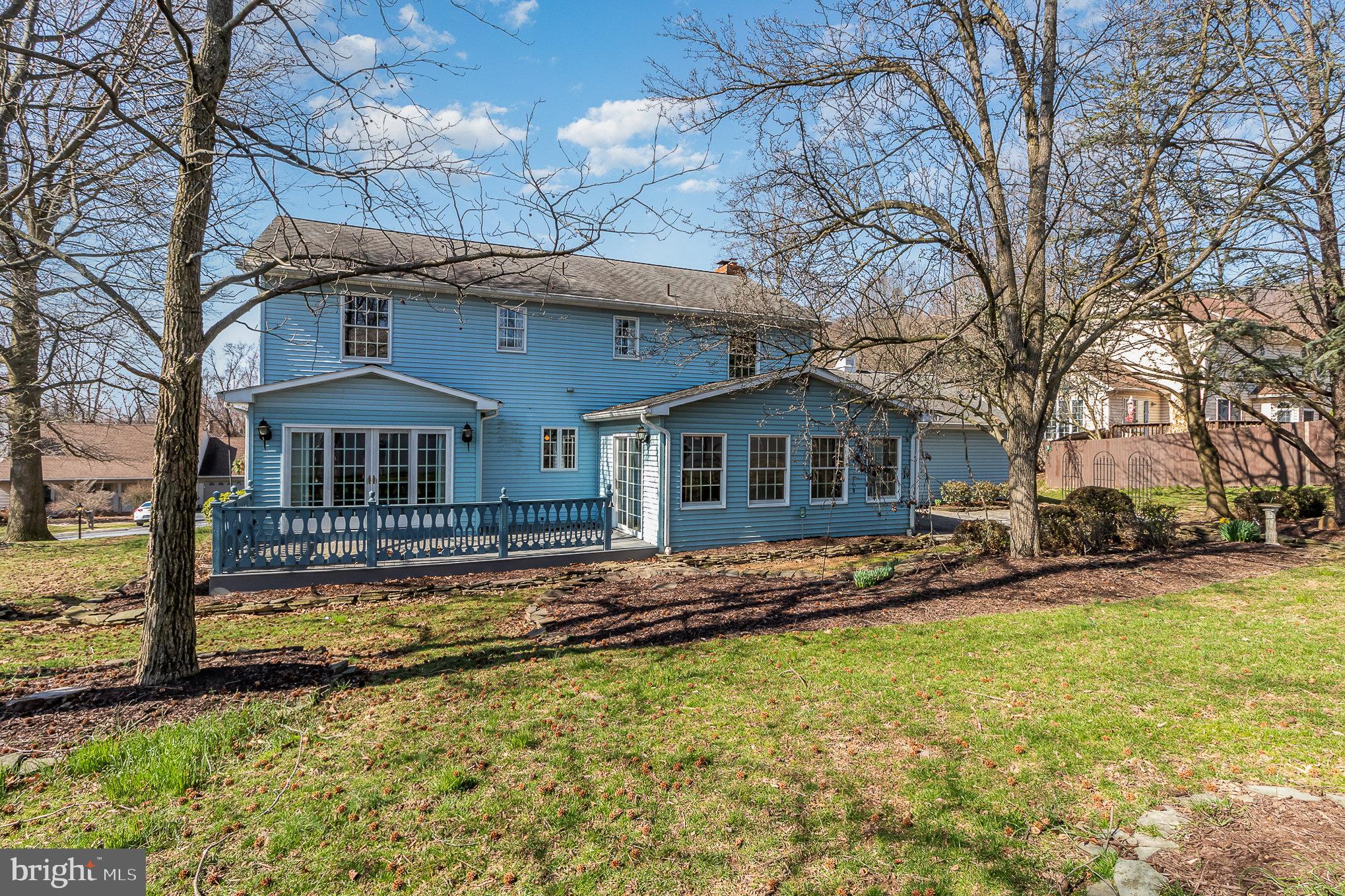 Blue two-story house with a raised deck and large windows, framed by leafless trees.