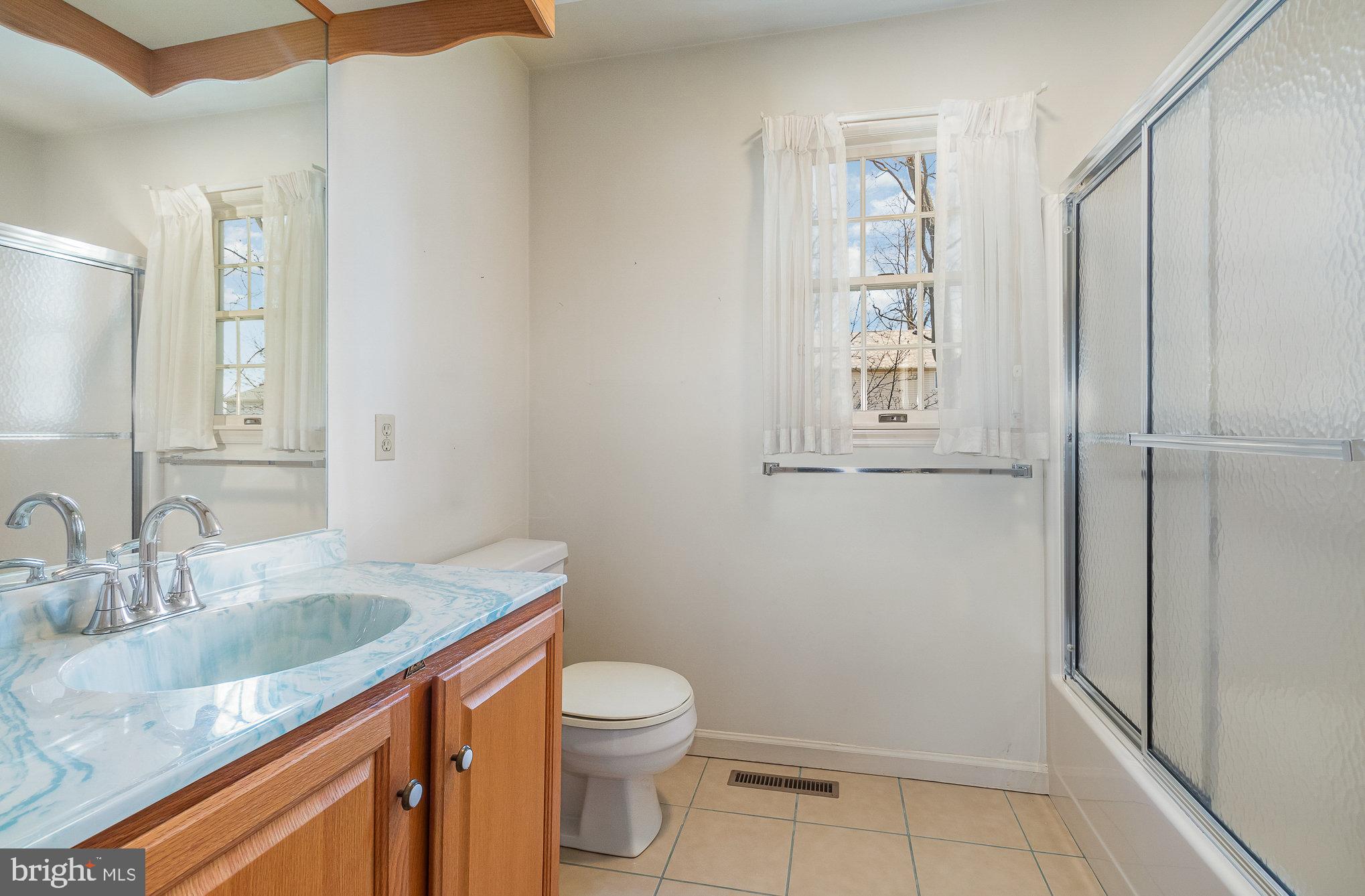 Bathroom with a wood vanity, blue marbled countertop, curtained window, and glass-enclosed shower.