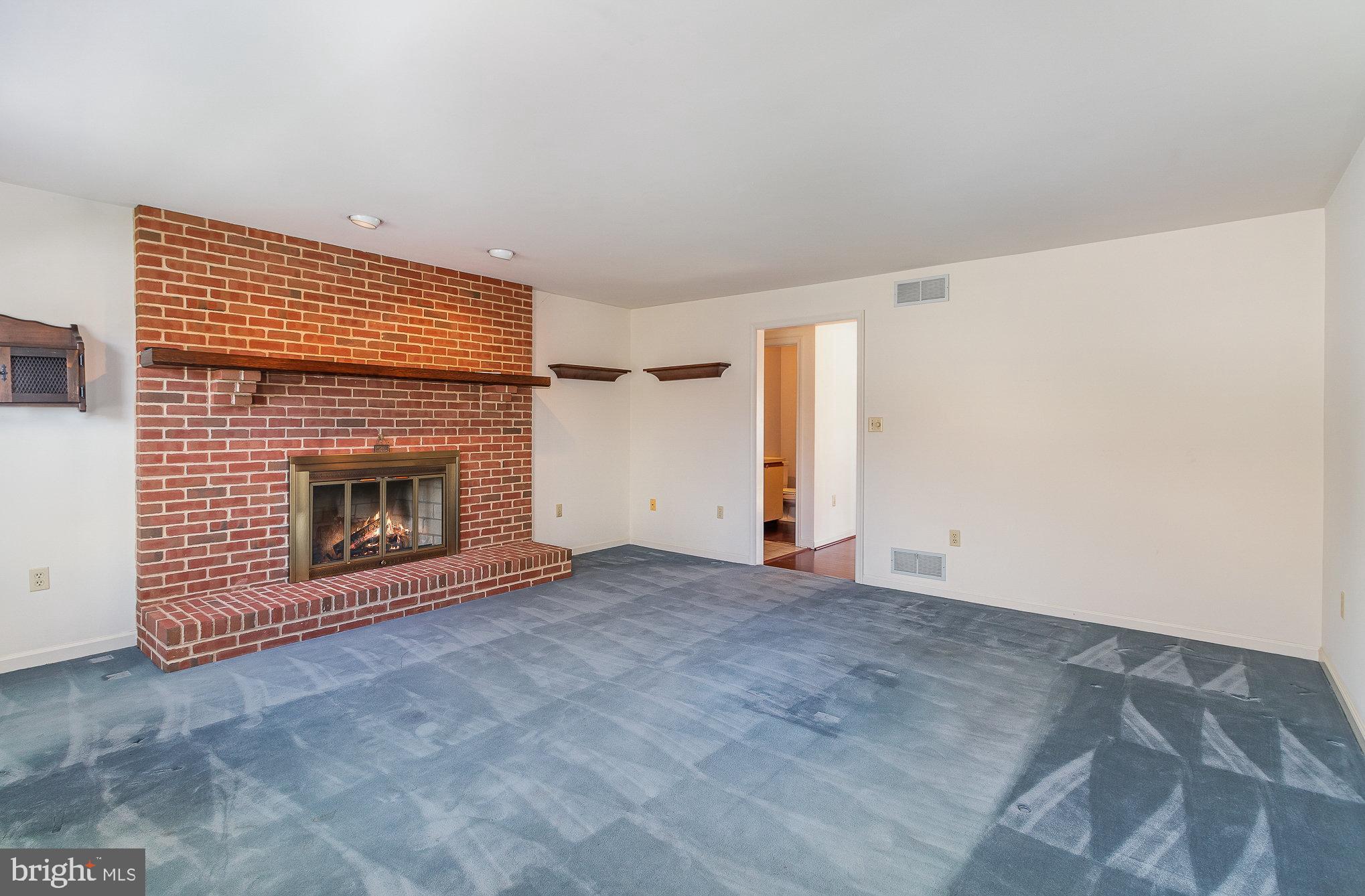 Empty living room with a red brick fireplace, raised hearth, and blue-gray carpet.