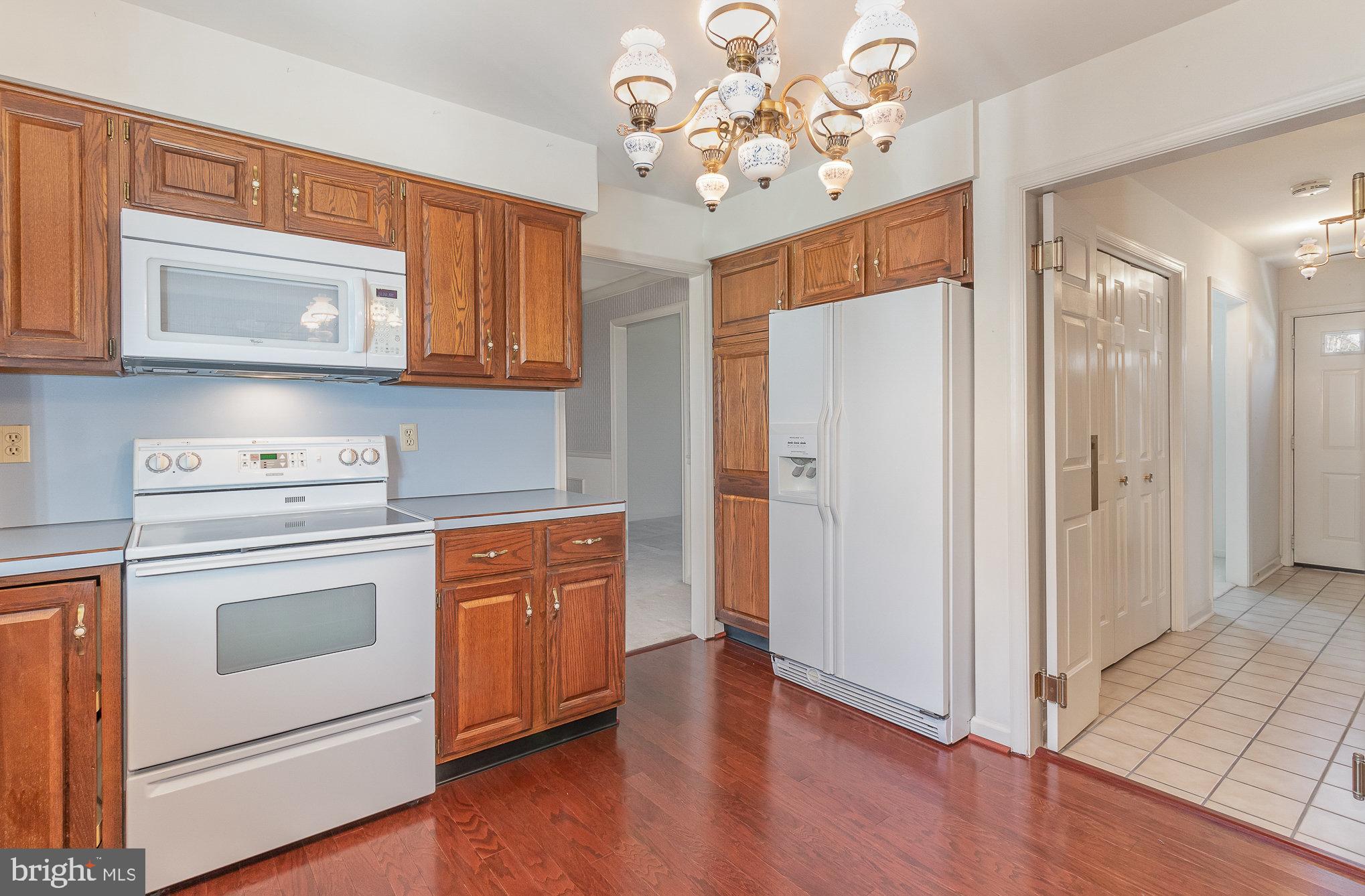 Kitchen with wood cabinets, white appliances, and a decorative chandelier.
