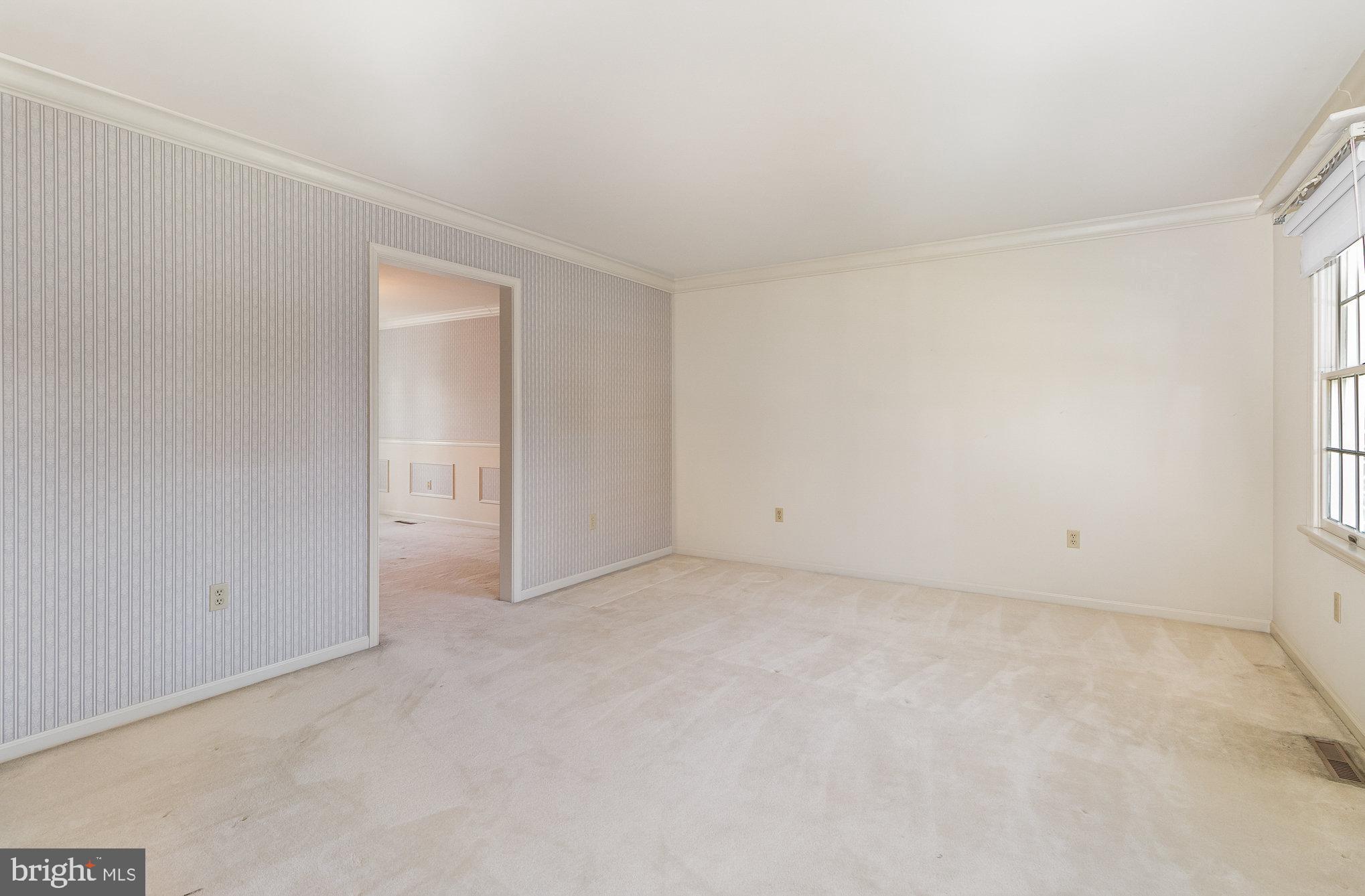Empty carpeted room with striped wallpaper, a large window, and an open doorway.