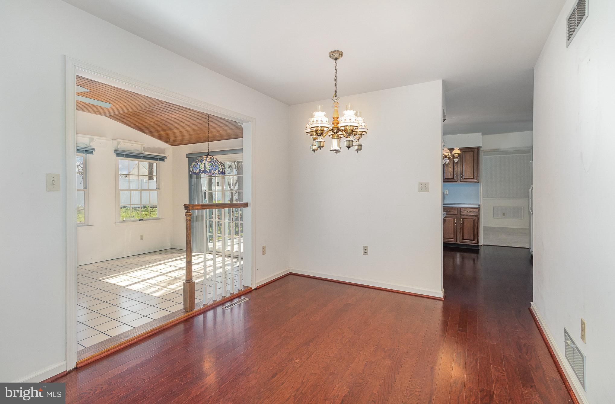 Empty dining room with hardwood floors and chandelier beside a bright tiled breakfast area.