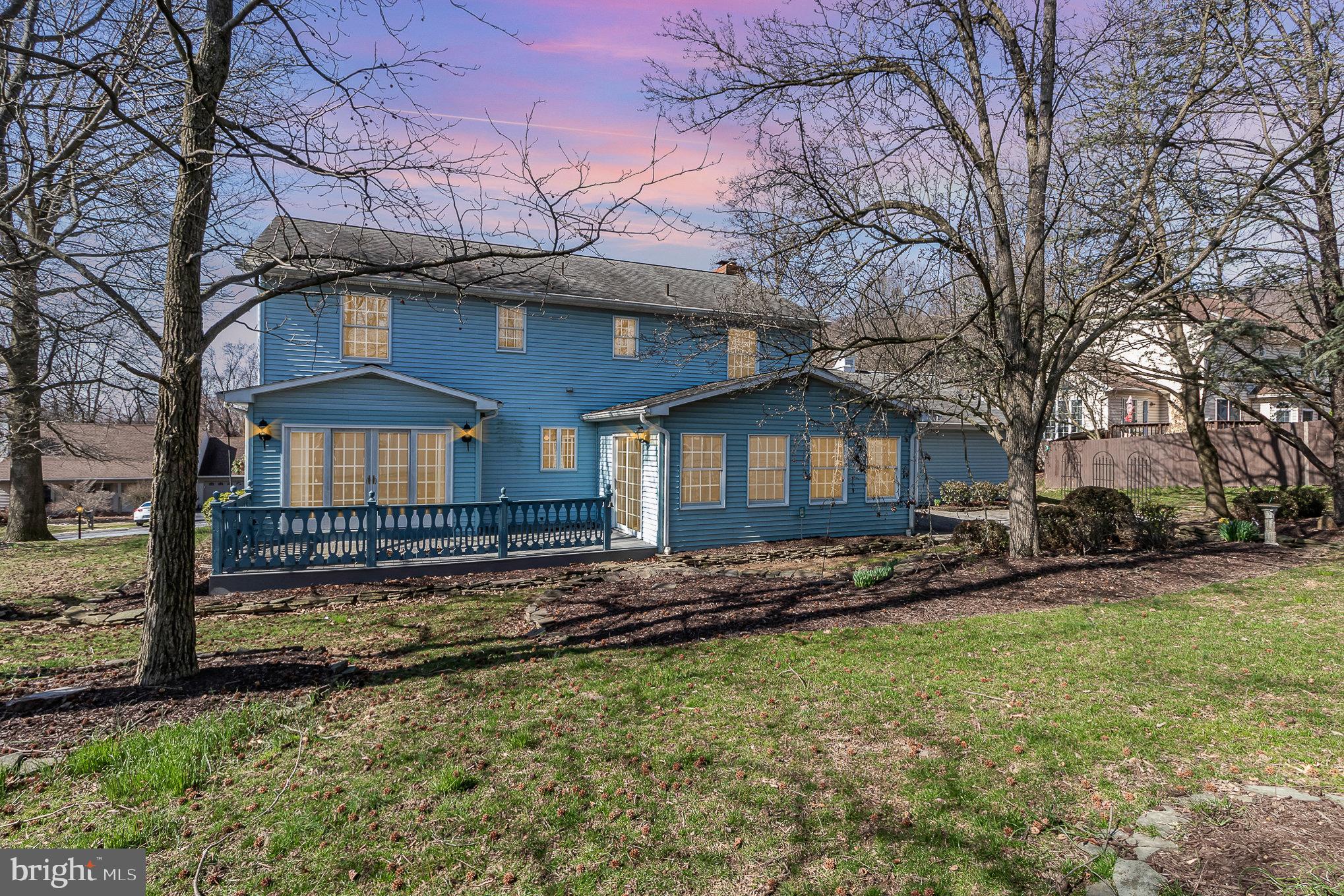 Two-story blue house with a raised deck and French doors, framed by leafless trees.