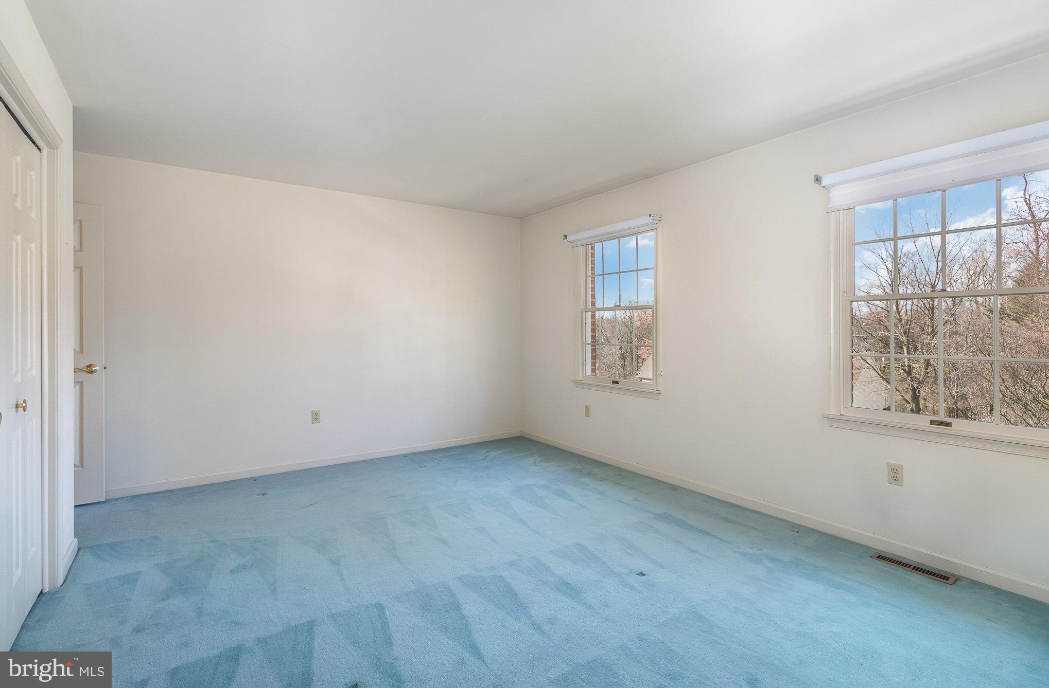 Empty room with blue carpet and two large windows overlooking bare trees.