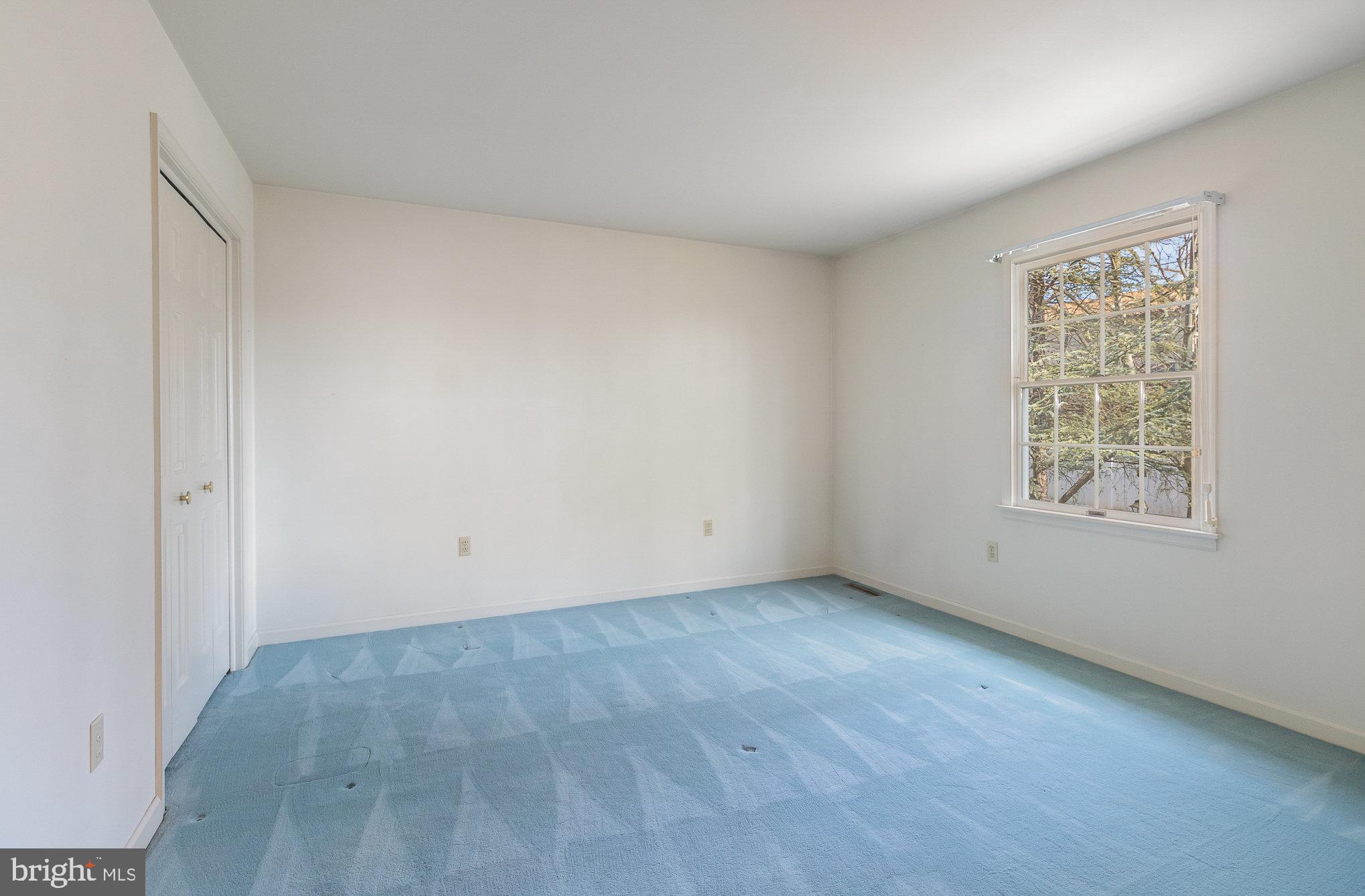 Empty bedroom with blue carpet, closet doors, and a large window overlooking trees.