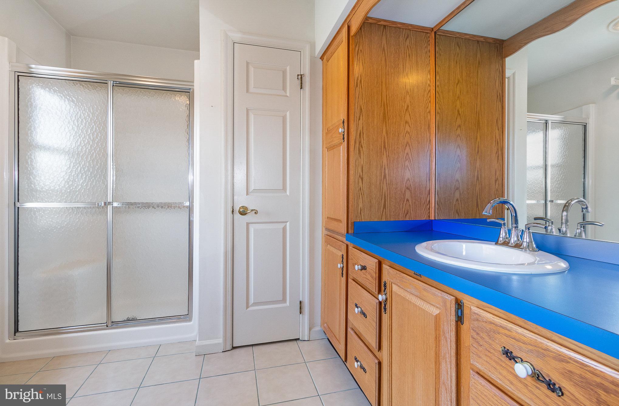 Bathroom with oak cabinets, a bright blue vanity countertop, and a glass-enclosed shower.