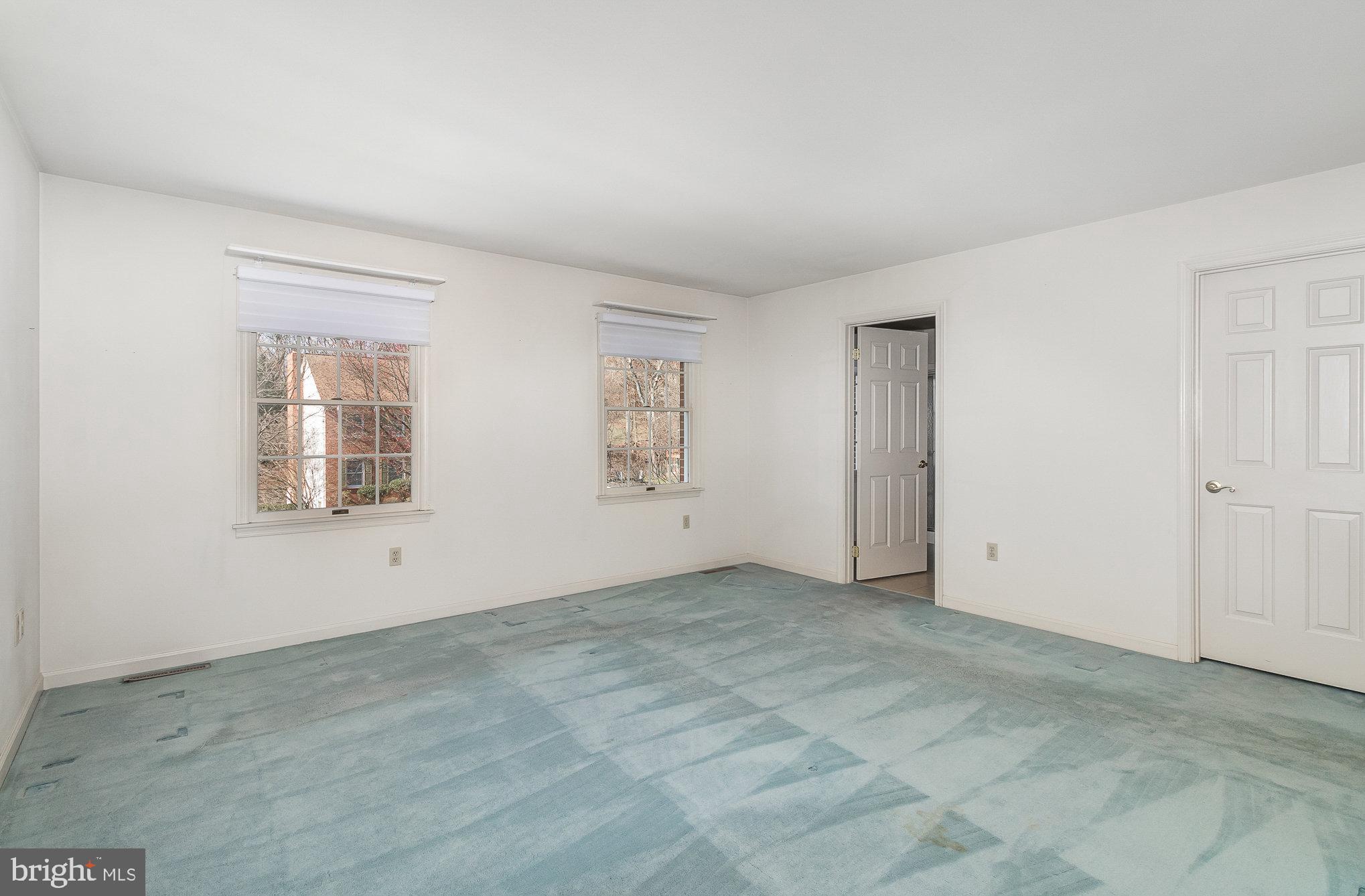 Empty room with pale blue carpet, two windows, and two white doors.