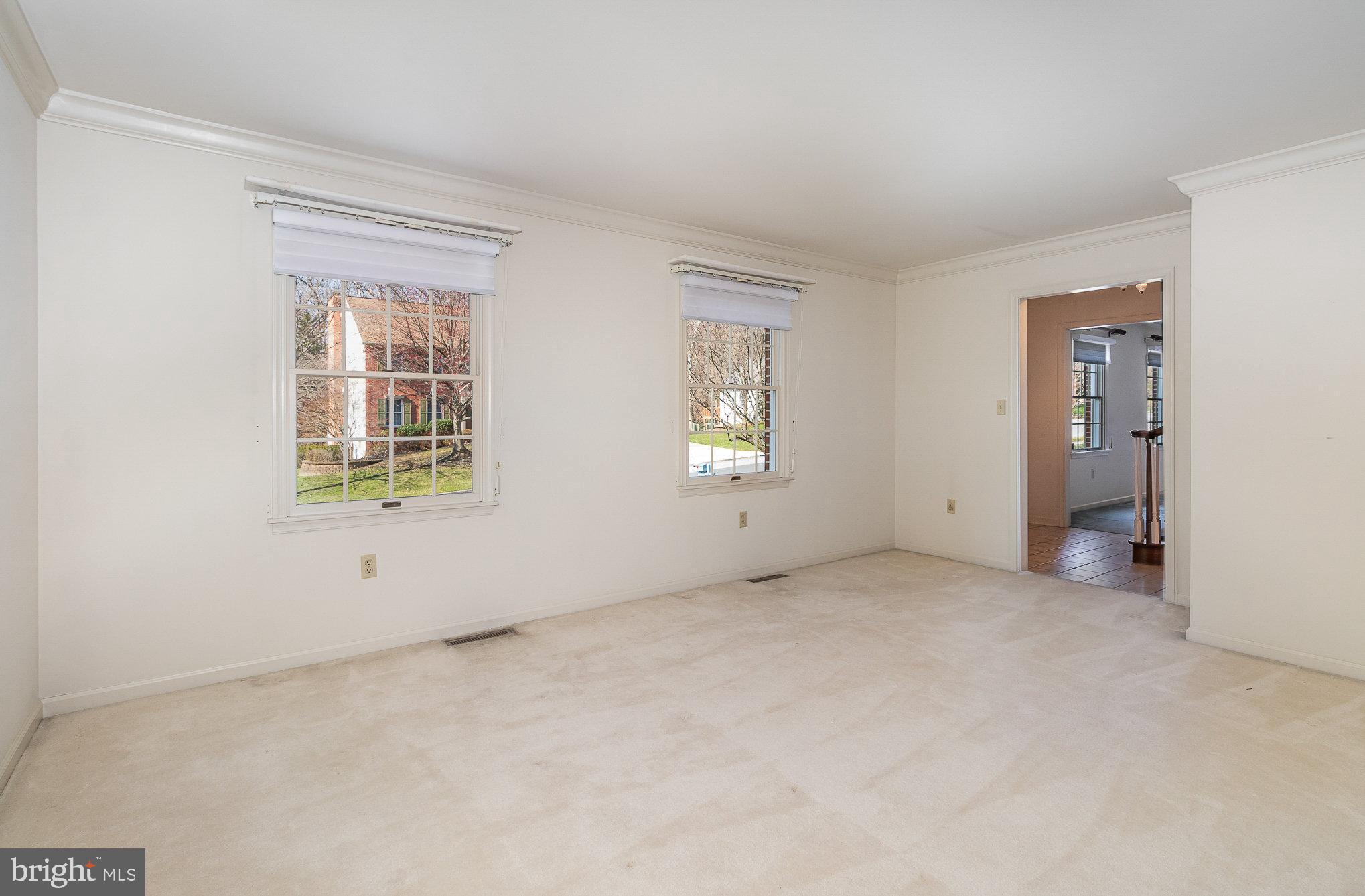 Empty carpeted room with two blind-covered windows and a doorway to a tiled adjoining area.